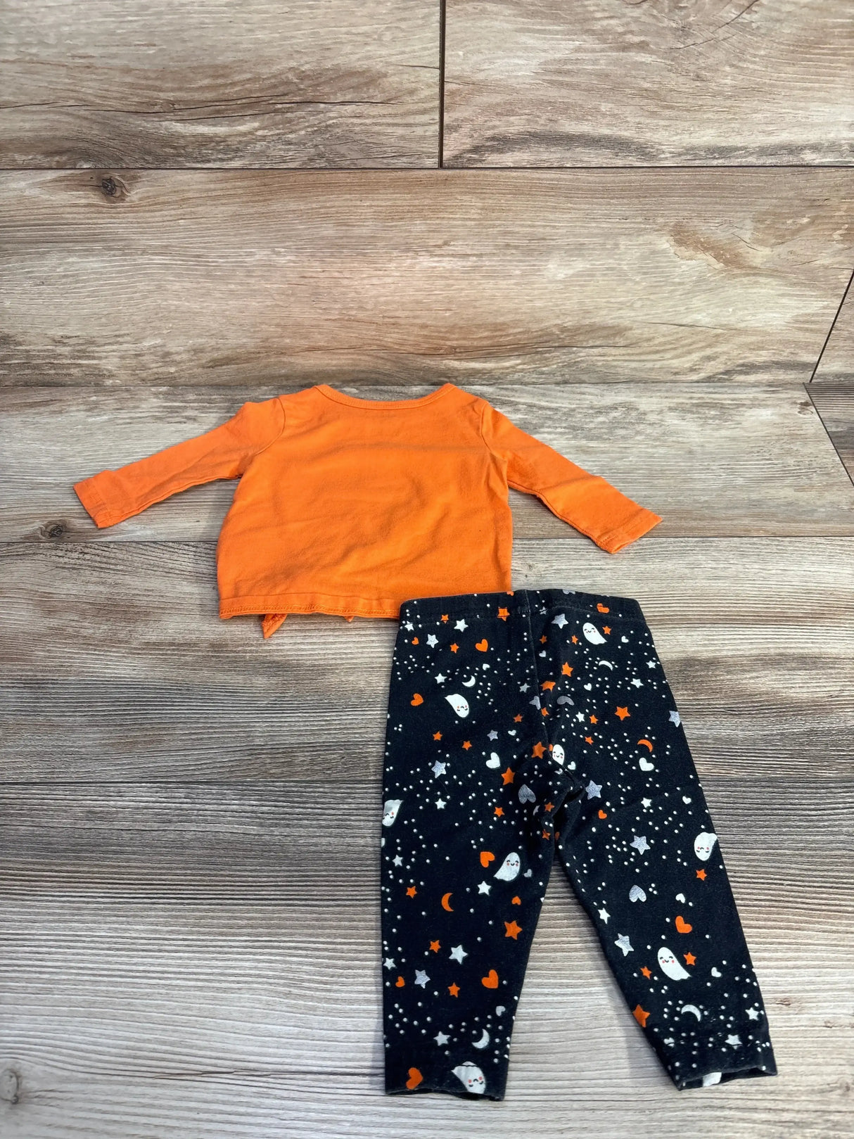 Top view of two piece Candy Corn shirt and leggings set showcasing an orange shirt and ghost print leggings on a wood floor