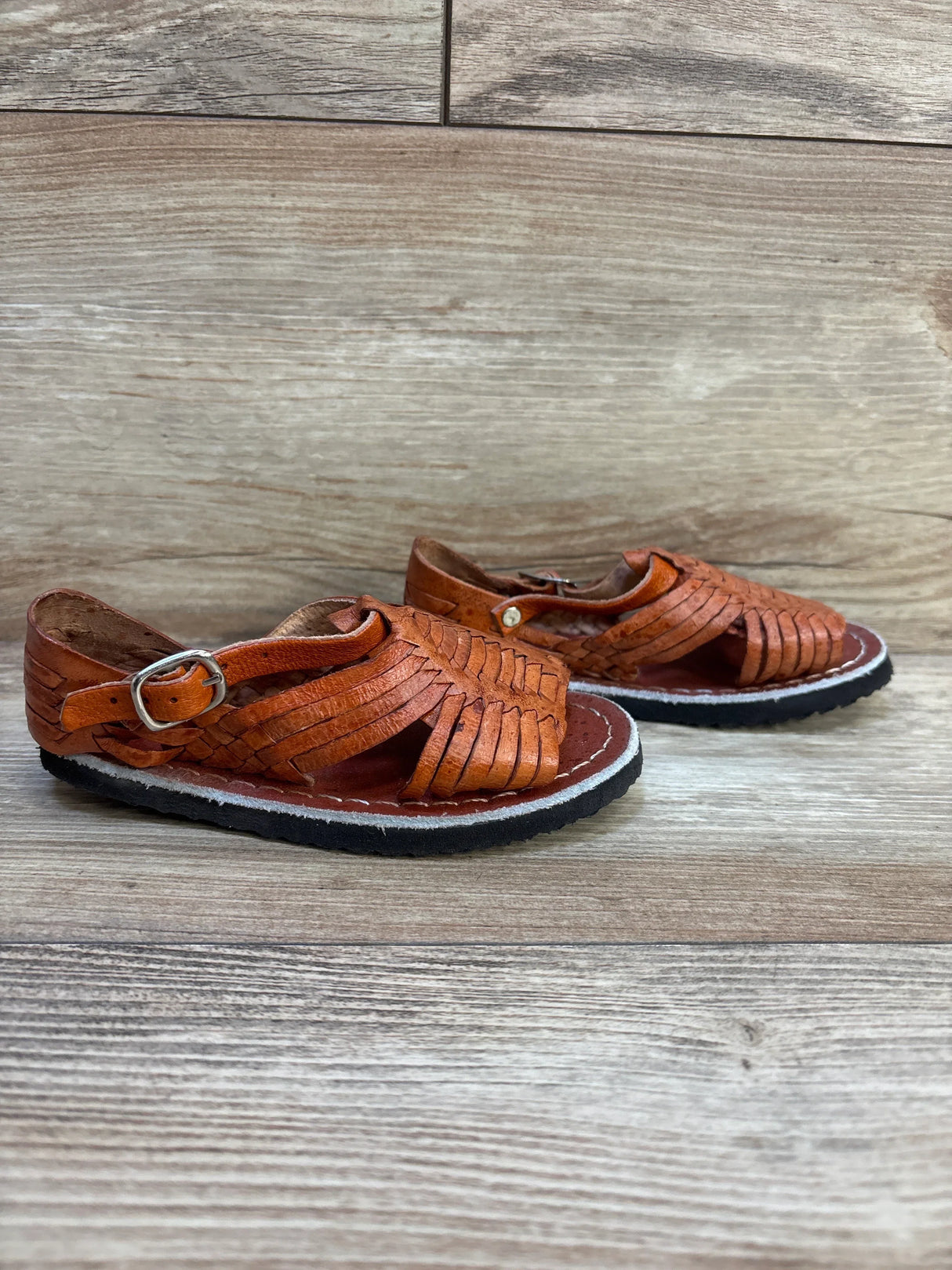 Brown woven leather toddler sandals with buckles on a wood floor