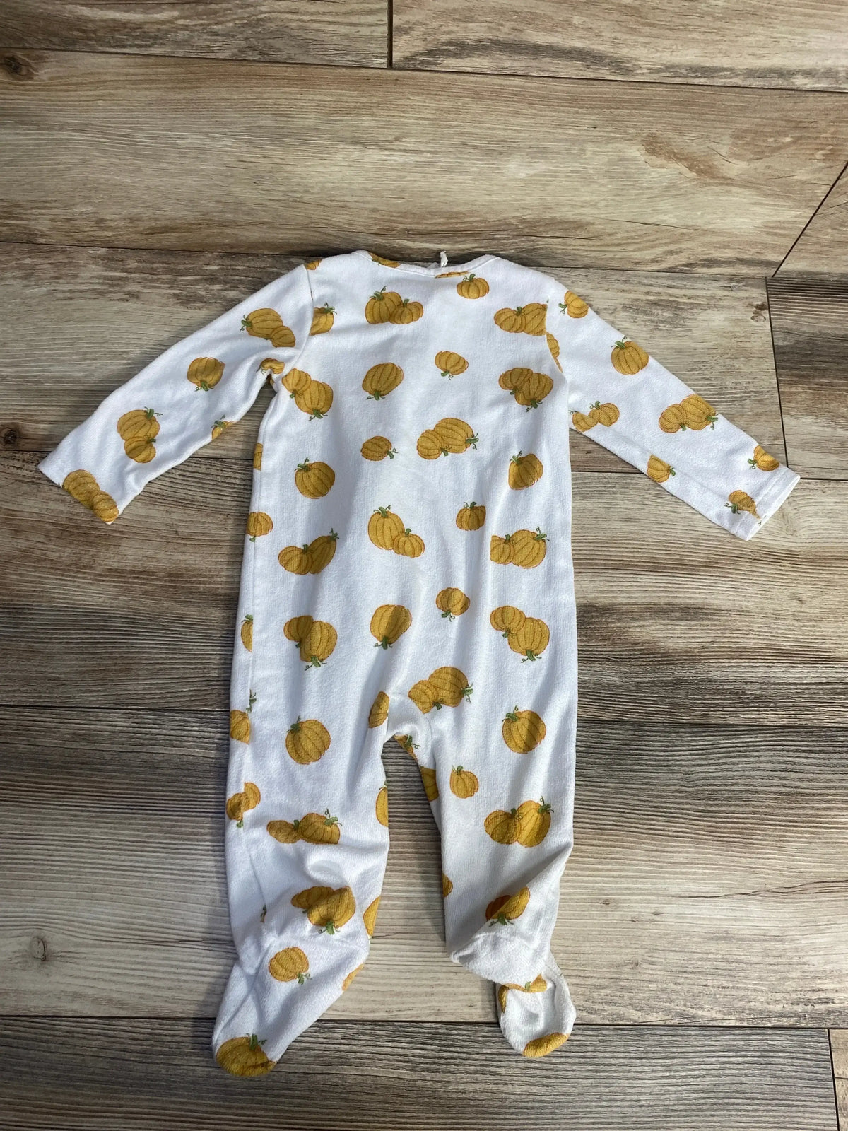 White baby onesie with yellow pumpkin pattern on wooden floor