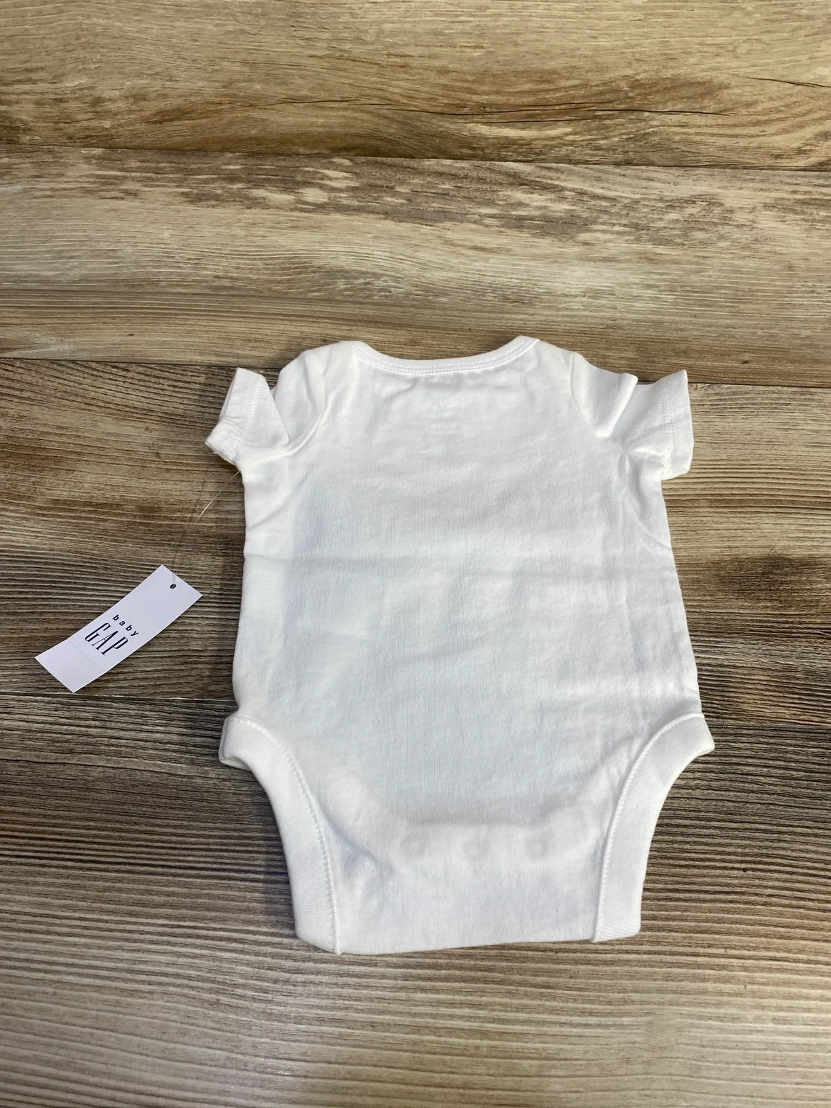 Back view of newborn white Baby Gap bodysuit showing short sleeves and brand tag on wood background