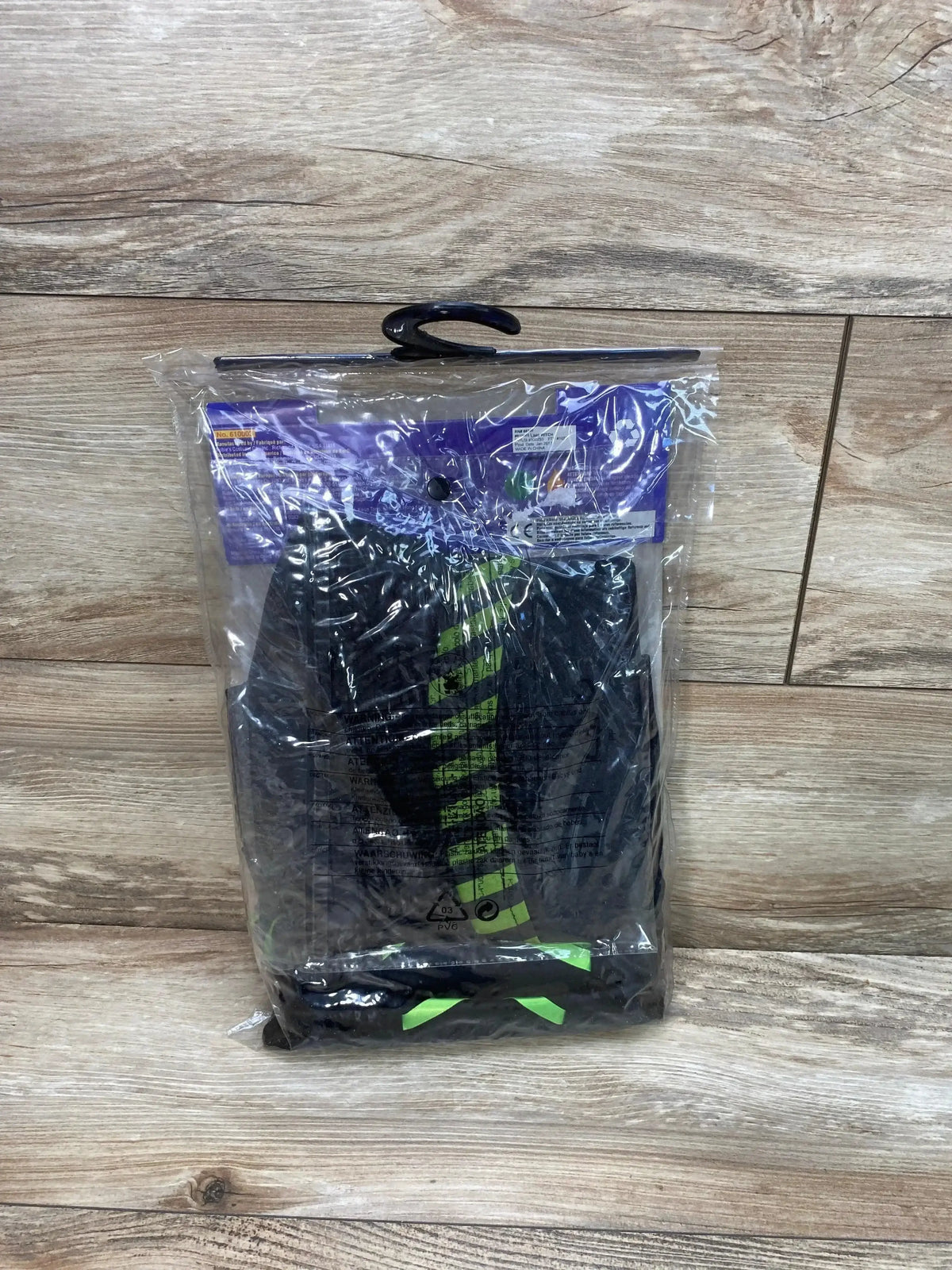 Front view of Rubie’s lime witch costume size 8-10 with lime-green stripes and bow in plastic packaging on wood background