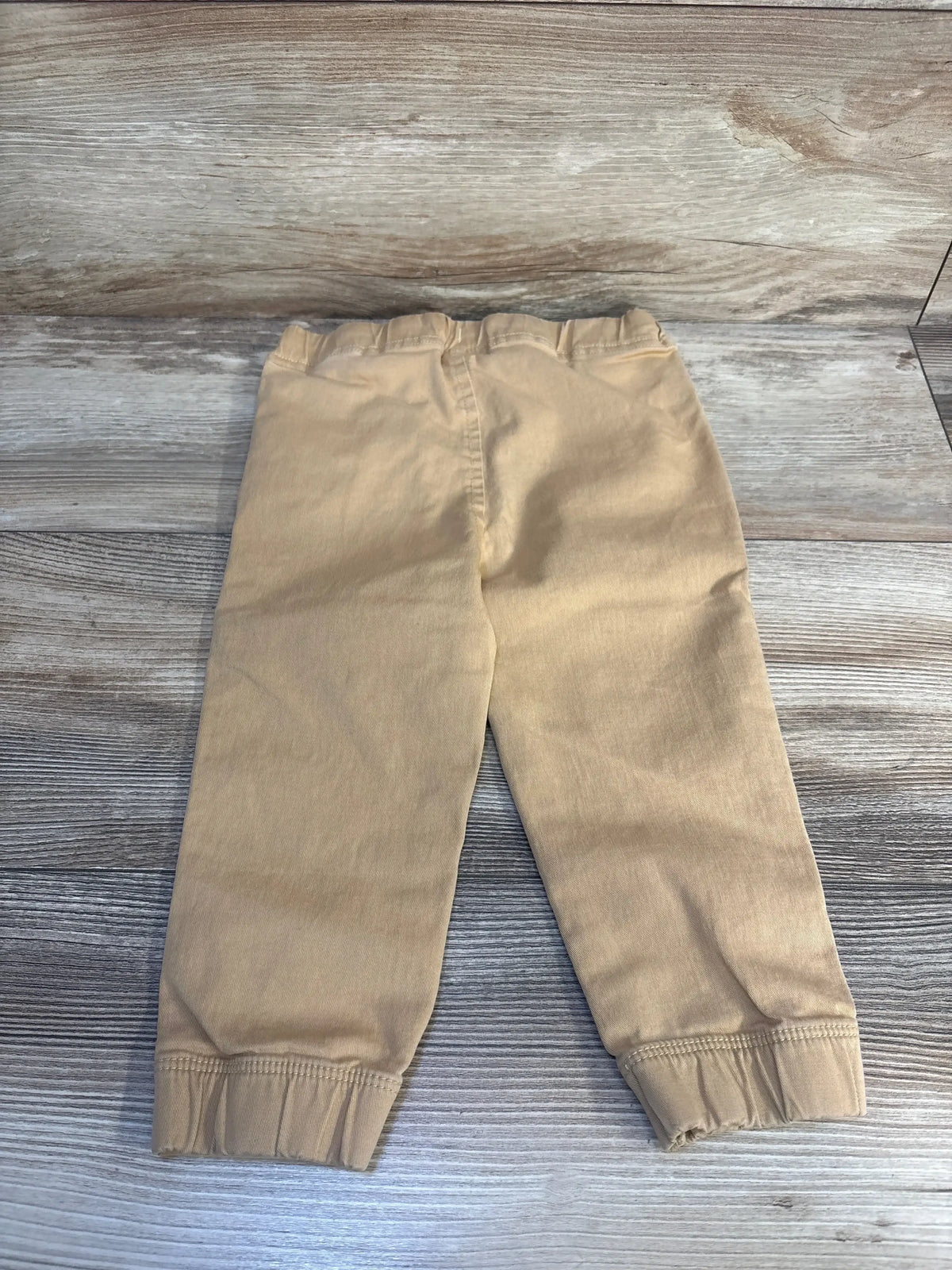 Flat lay of Ever & Ever tan toddler drawstring joggers size 2T showing elastic waistband and cuffed ankles on wood background