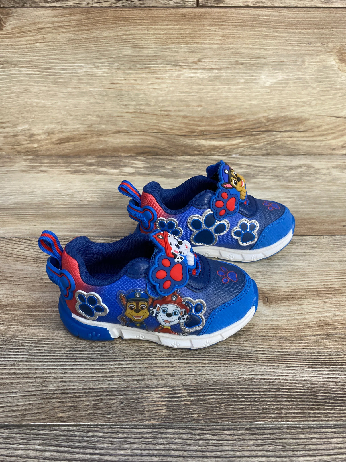 Blue kids sneakers with Paw Patrol characters and paw prints on wooden floor