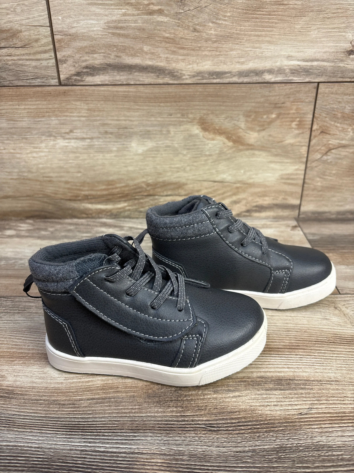 Black kids high-top sneakers with grey padded collar and white sole on wooden floor