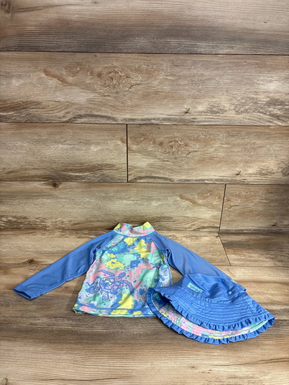 Front view of blue UV Skinz rash guard shirt and bucket hat set showcasing long sleeves and colorful shirt front on a wood floor