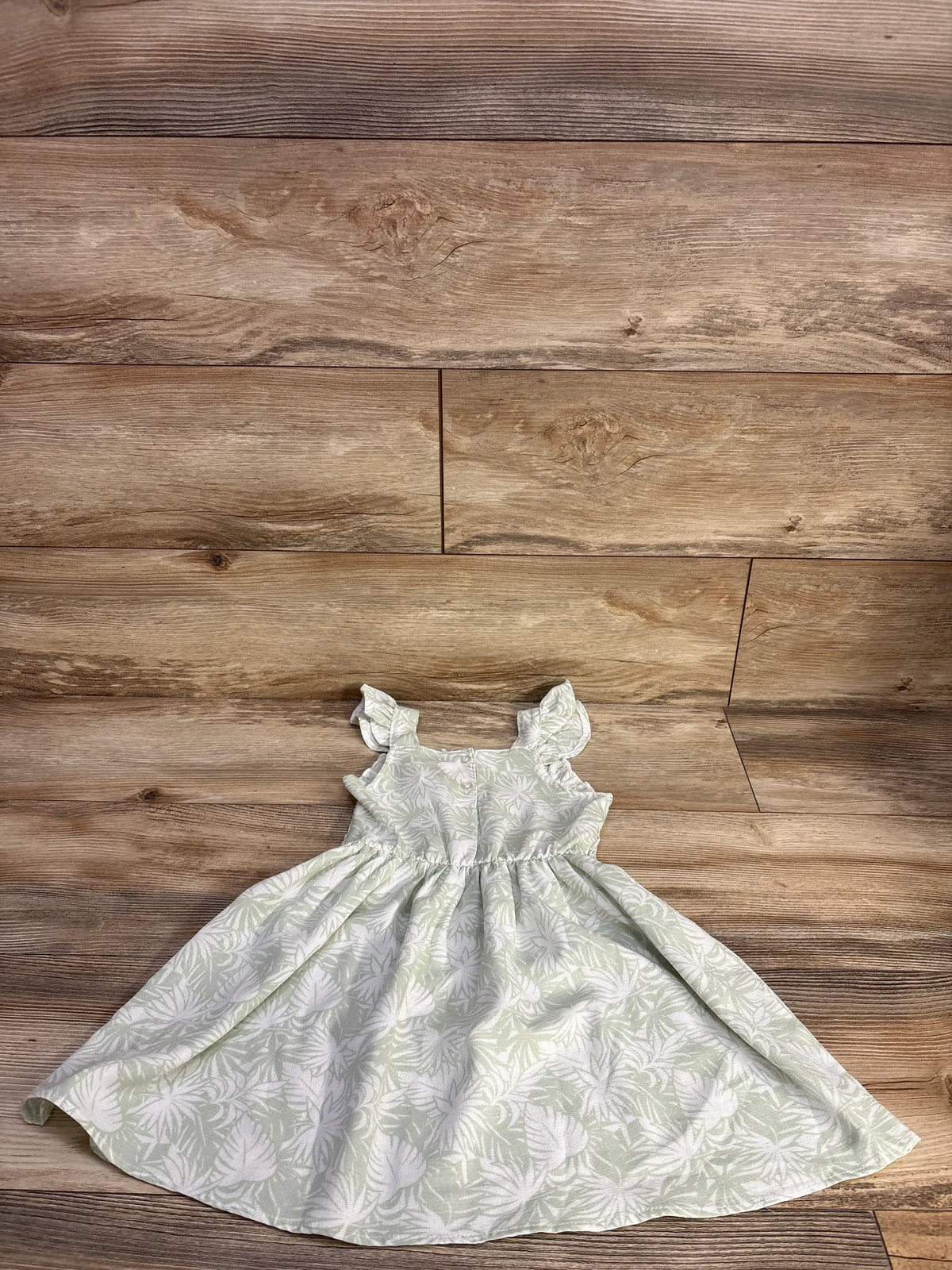 Flat lay of Little Lass smocked girls' dress in pale green with white leaf print, ruffle sleeves, gathered skirt, 4T