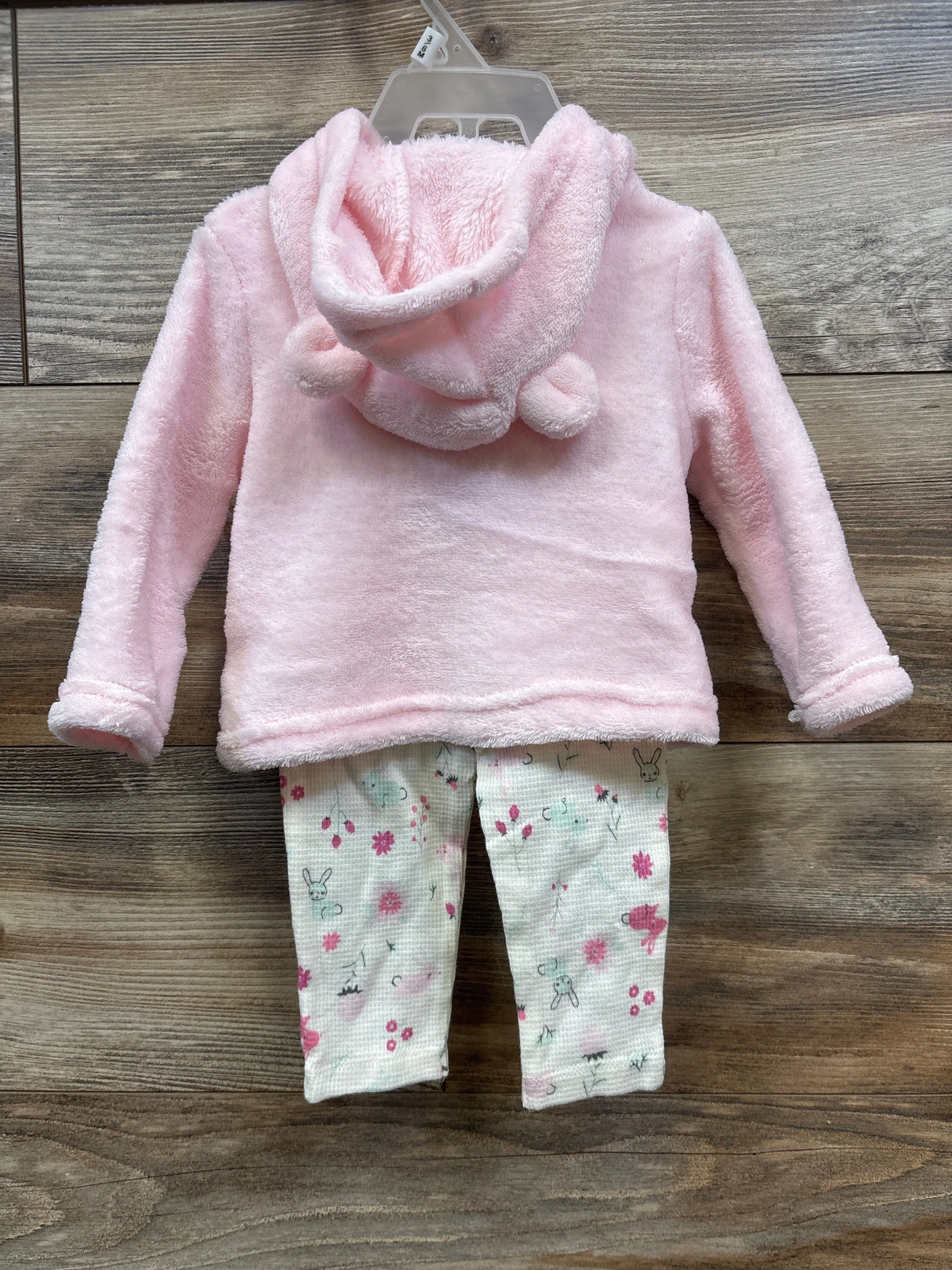 Back view of baby outfit with soft pink hooded jacket and white floral patterned pants on wooden floor