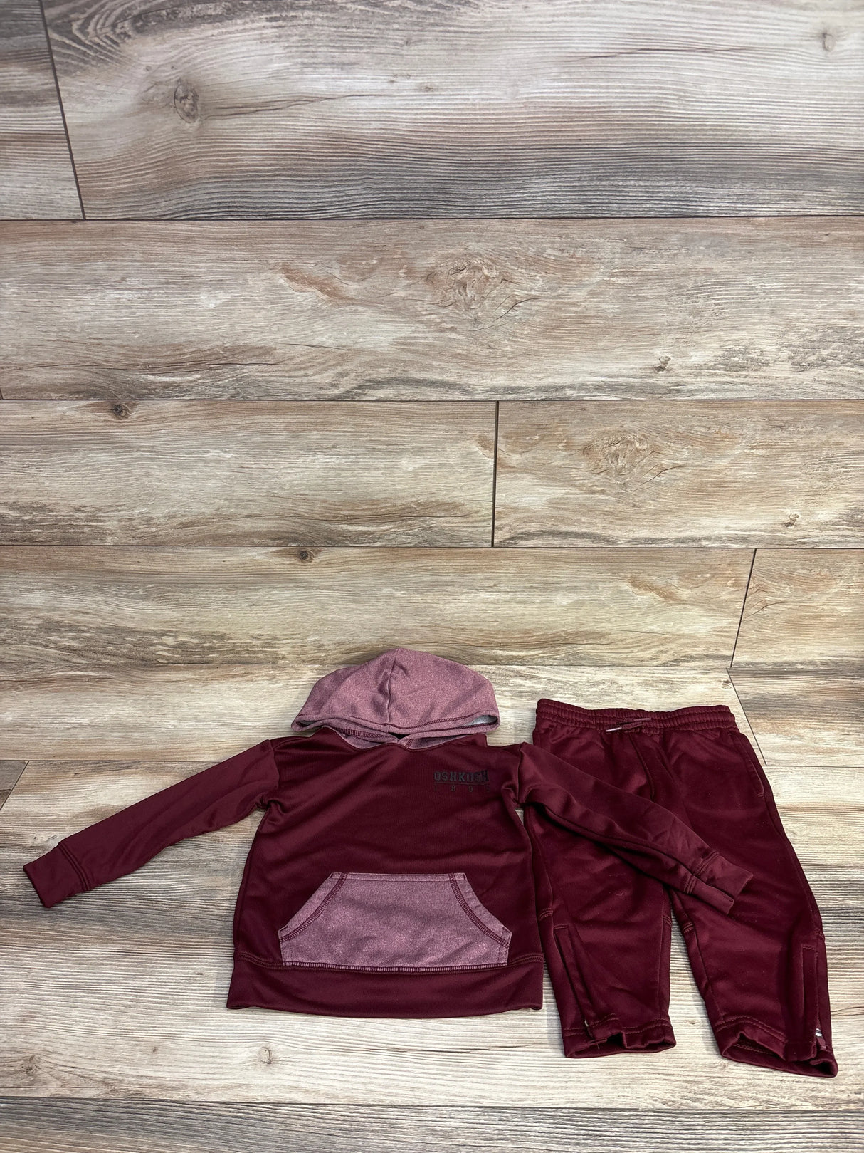 Children's maroon two-piece hooded sweatshirt and sweatpants set with contrasting pocket on wood floor