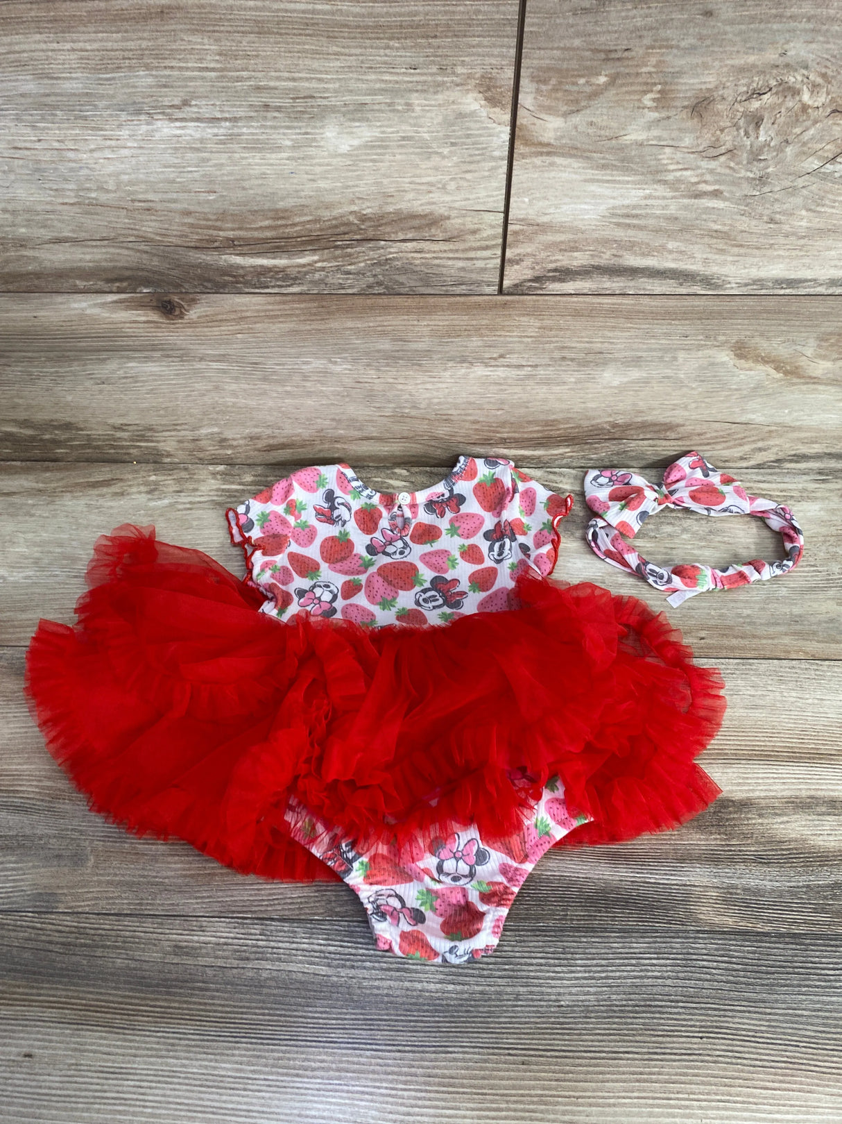 Baby girl strawberry and Minnie Mouse print dress with red tutu skirt and matching headband on wooden floor