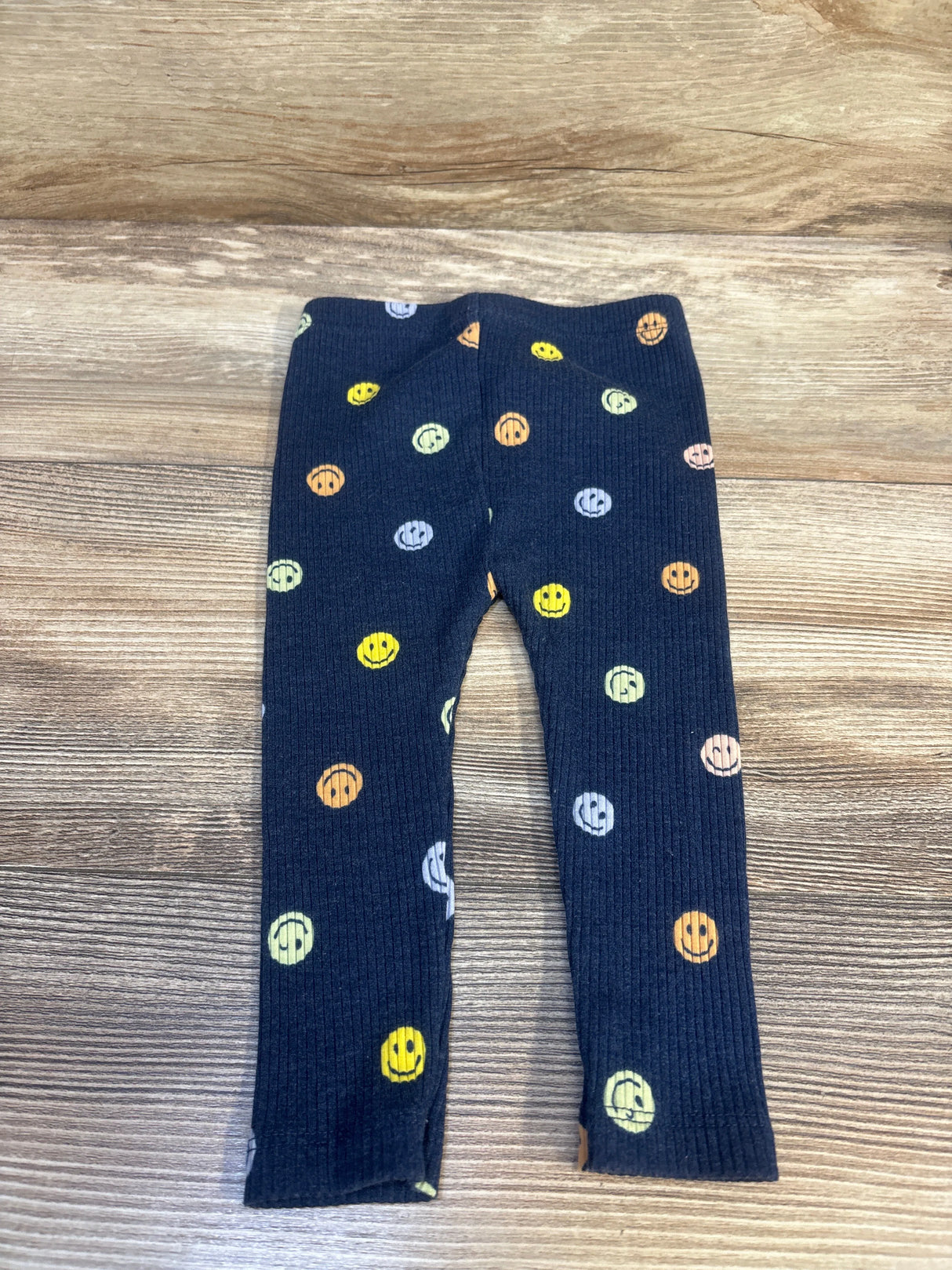 Flat lay of navy ribbed baby leggings showcasing multicolored smiley face print with wood tabletop background