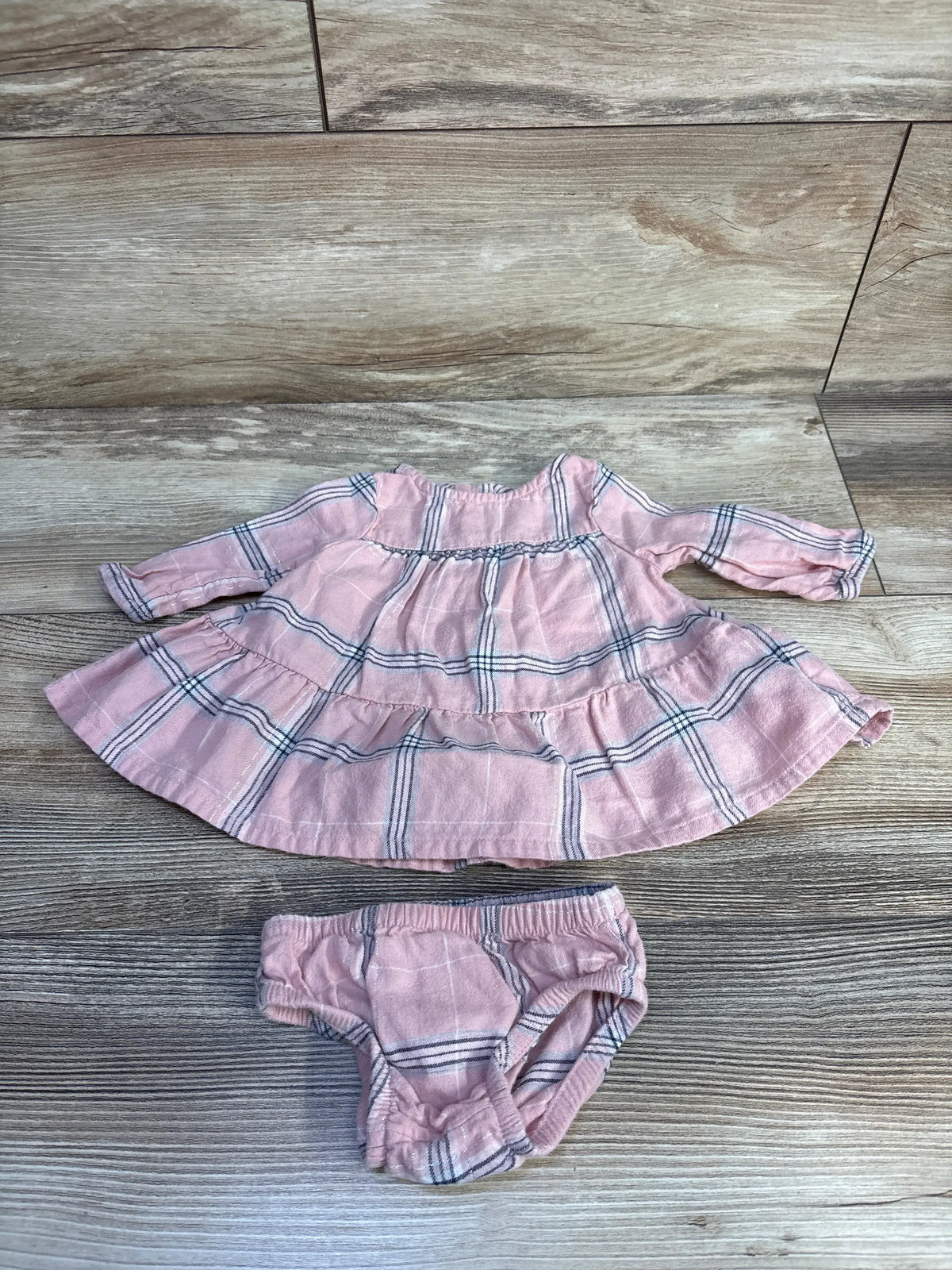 Front view of Carter’s pink newborn dress and matching bloomers set showcasing long sleeves and plaid pattern on a wood-look floor