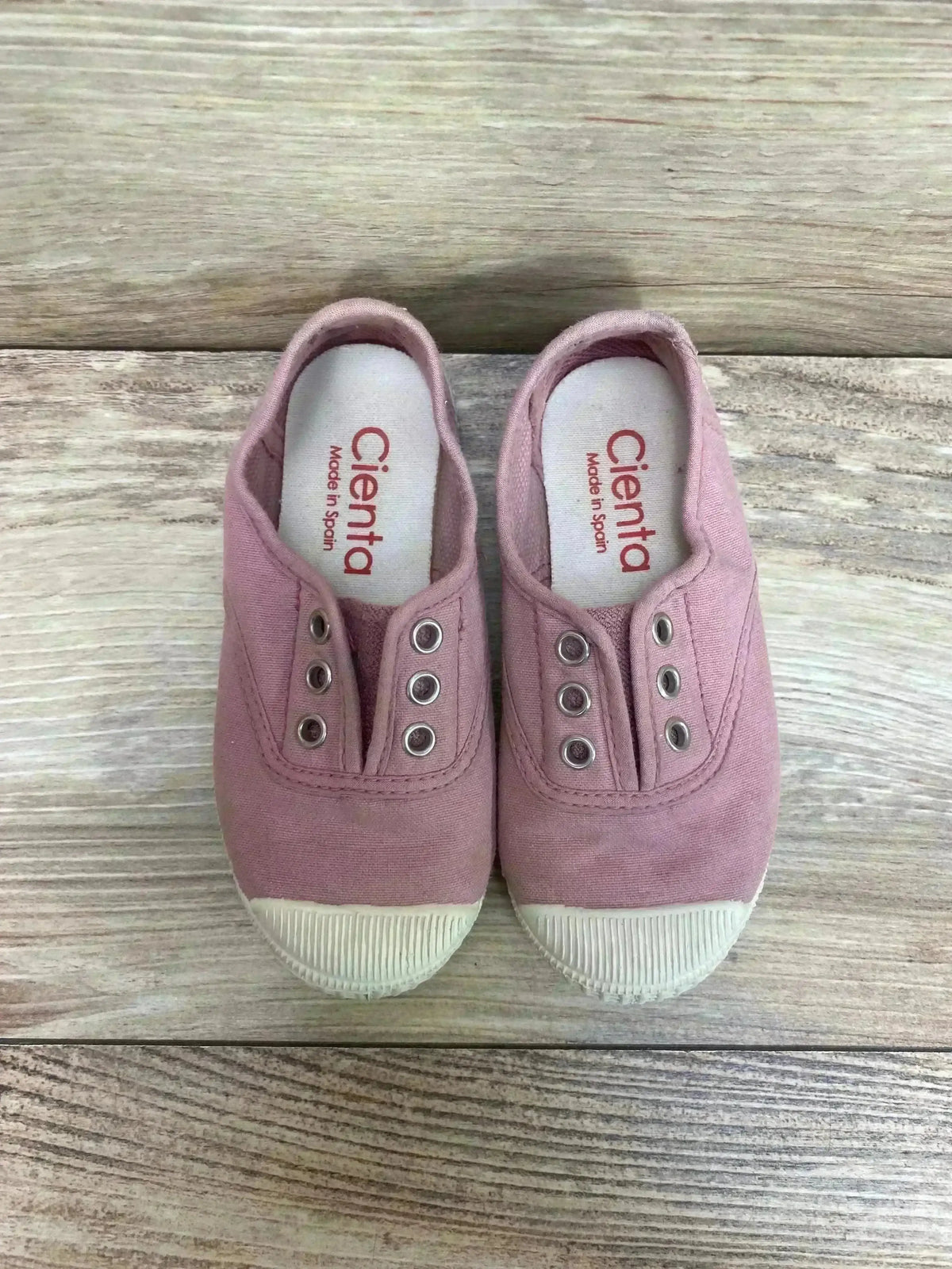 Top view of pink Cienta distressed canvas slip-on sneakers, size 9C, with elastic openings and rubber toe caps on wood grain