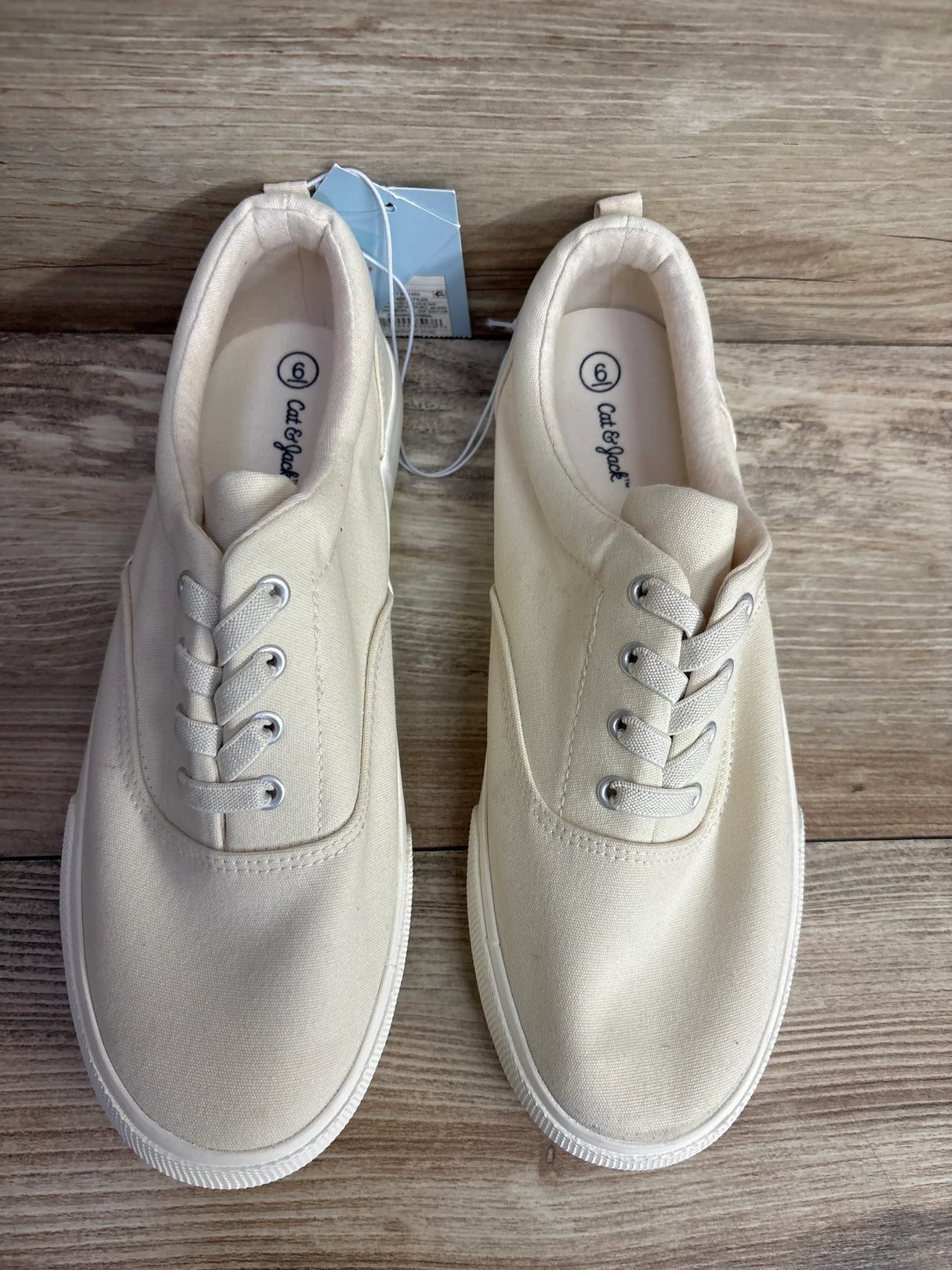 Cream canvas lace-up sneakers for kids with white soles on wooden floor