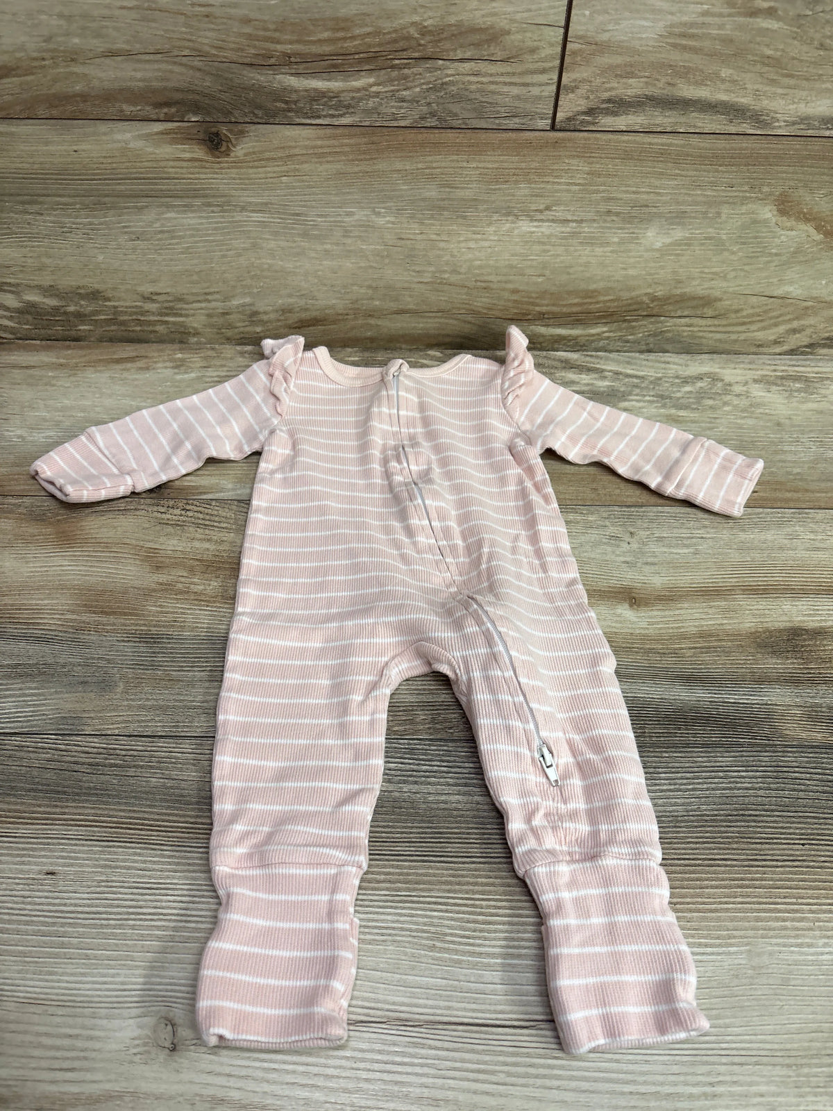 Pink organic ribbed baby sleeper with white stripes and ruffle shoulders on a wooden floor.