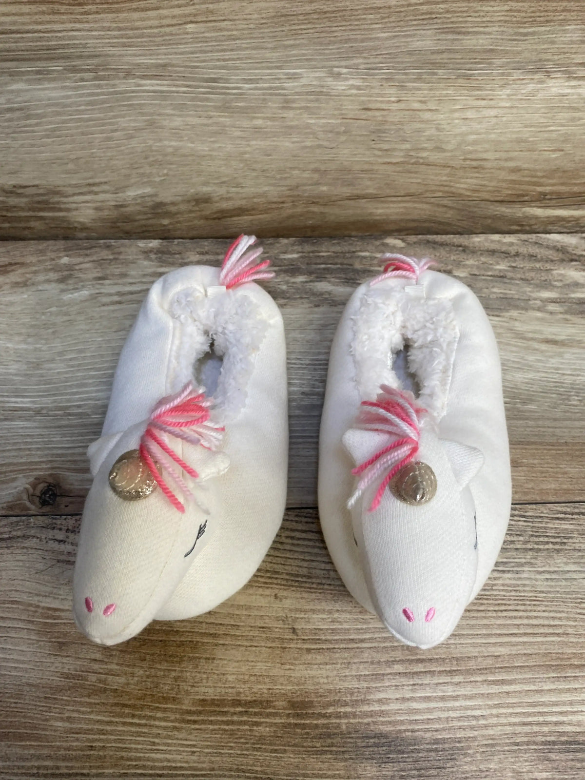 White unicorn baby slippers with pink manes and gold details on wooden background