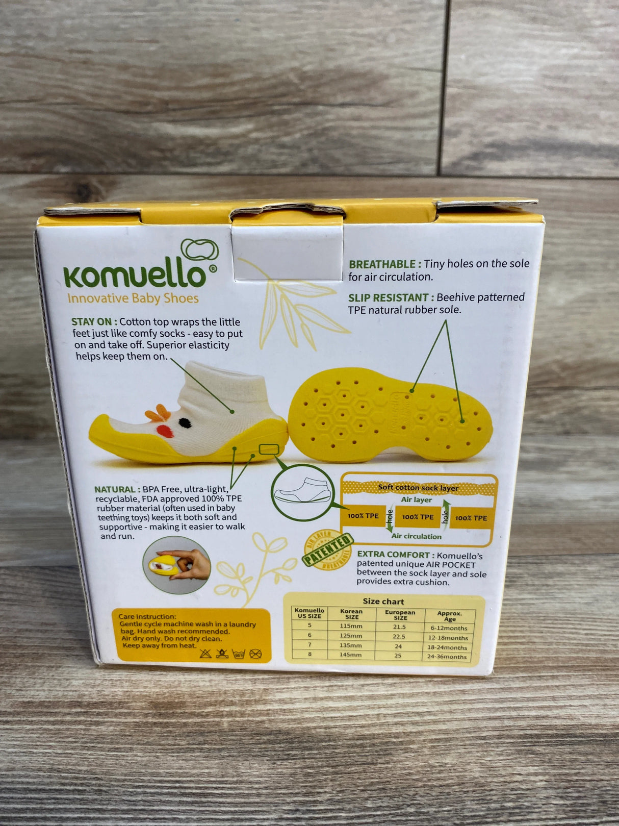 Box of Komuello innovative baby shoes with product features and size chart on wood background