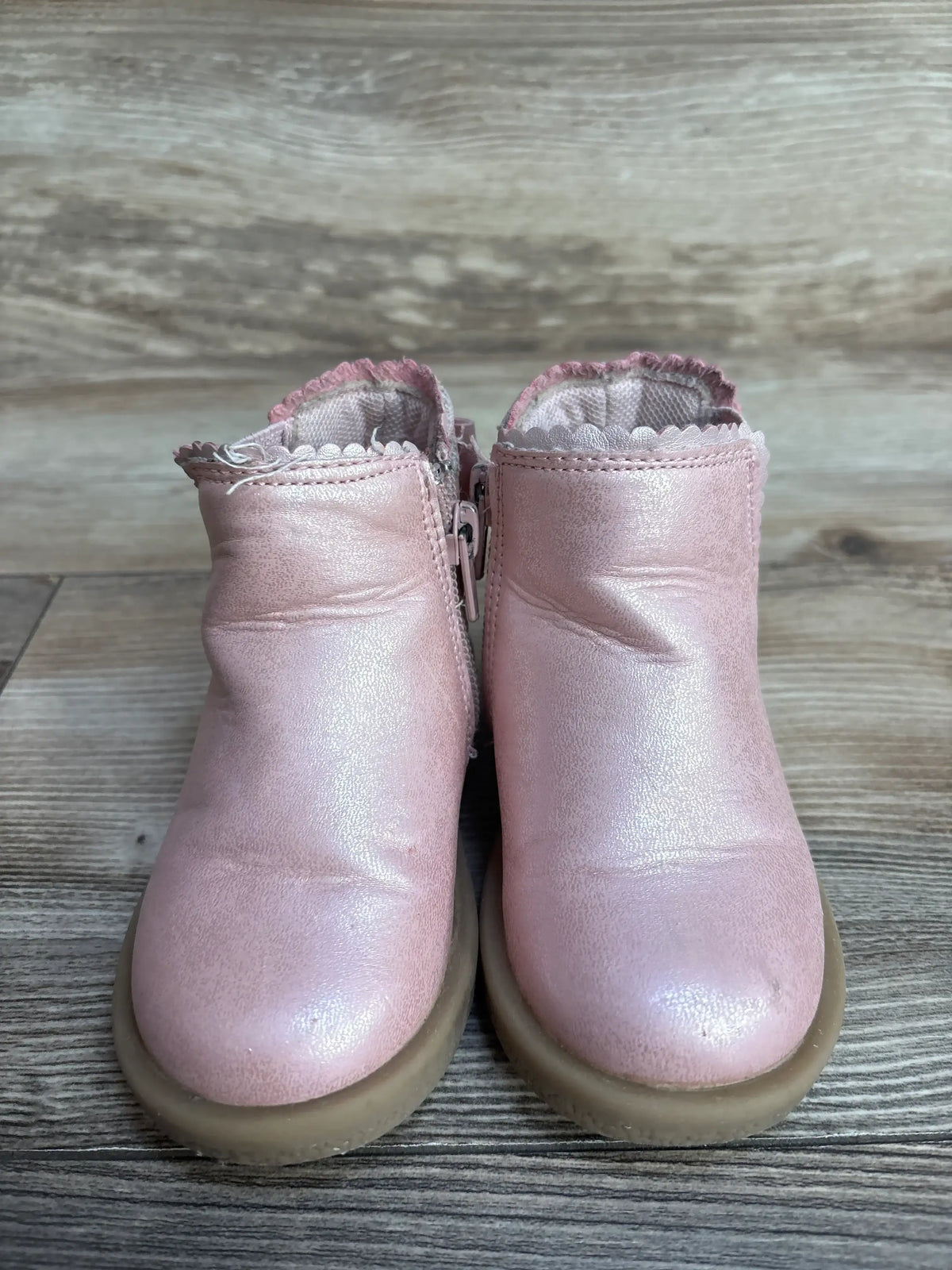 Pair of toddler pink leather boots with scalloped edges and rubber soles on wooden floor
