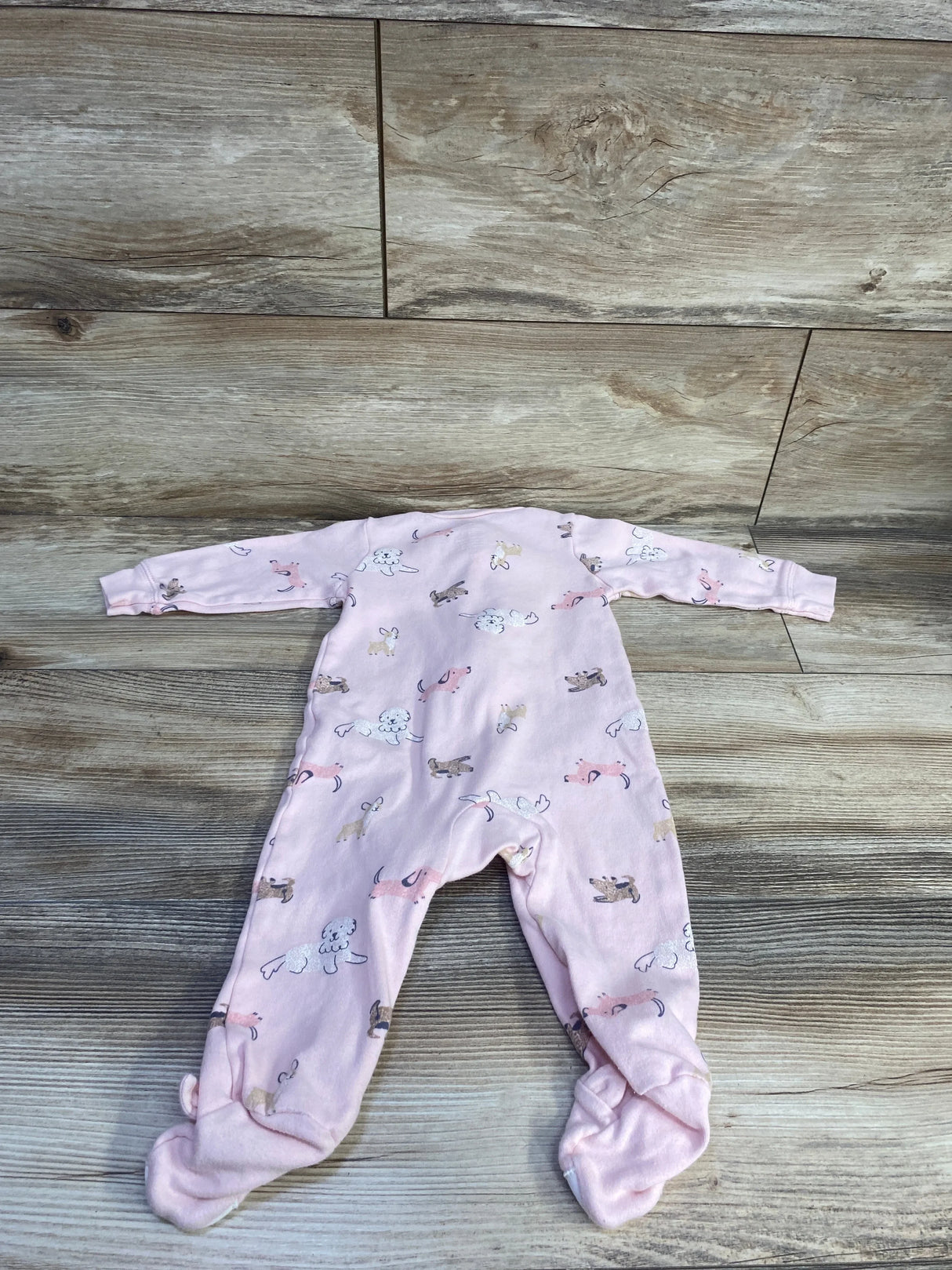 Flat lay of Carter's pink dog-print footed baby sleeper (size 9 months) showcasing long sleeves and all-over dog pattern on wood background