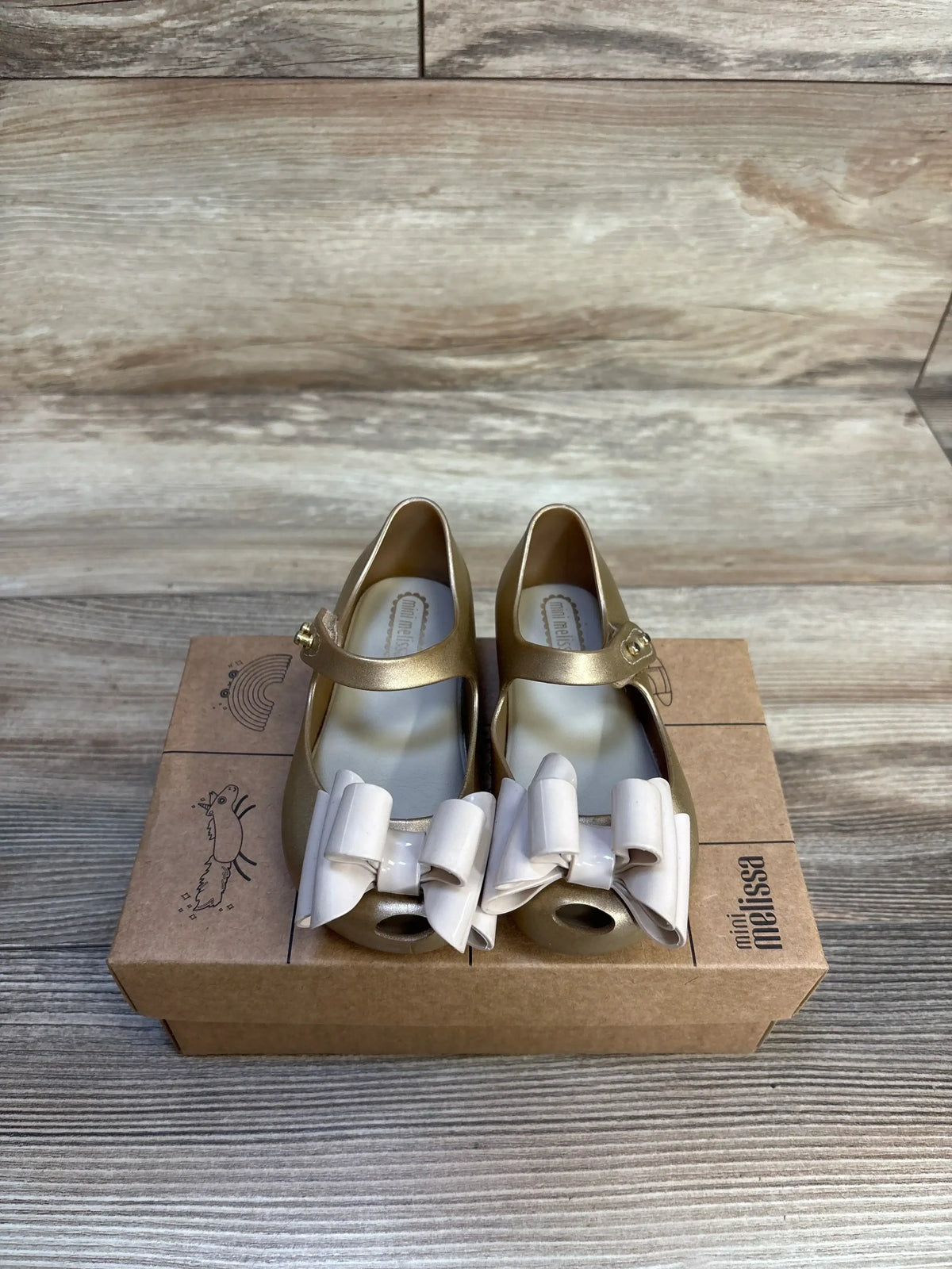 Top view of Mini Melissa Ultragirl Sweet Mary Jane shoes, size 7C, showing white bow accents and Mary Jane strap on cardboard box