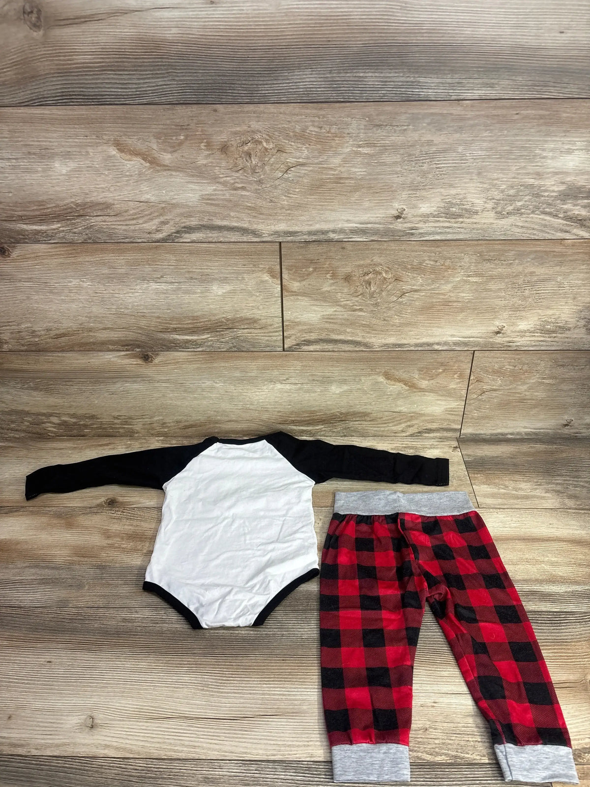 Baby onesie with black sleeves and red plaid pants on wood floor