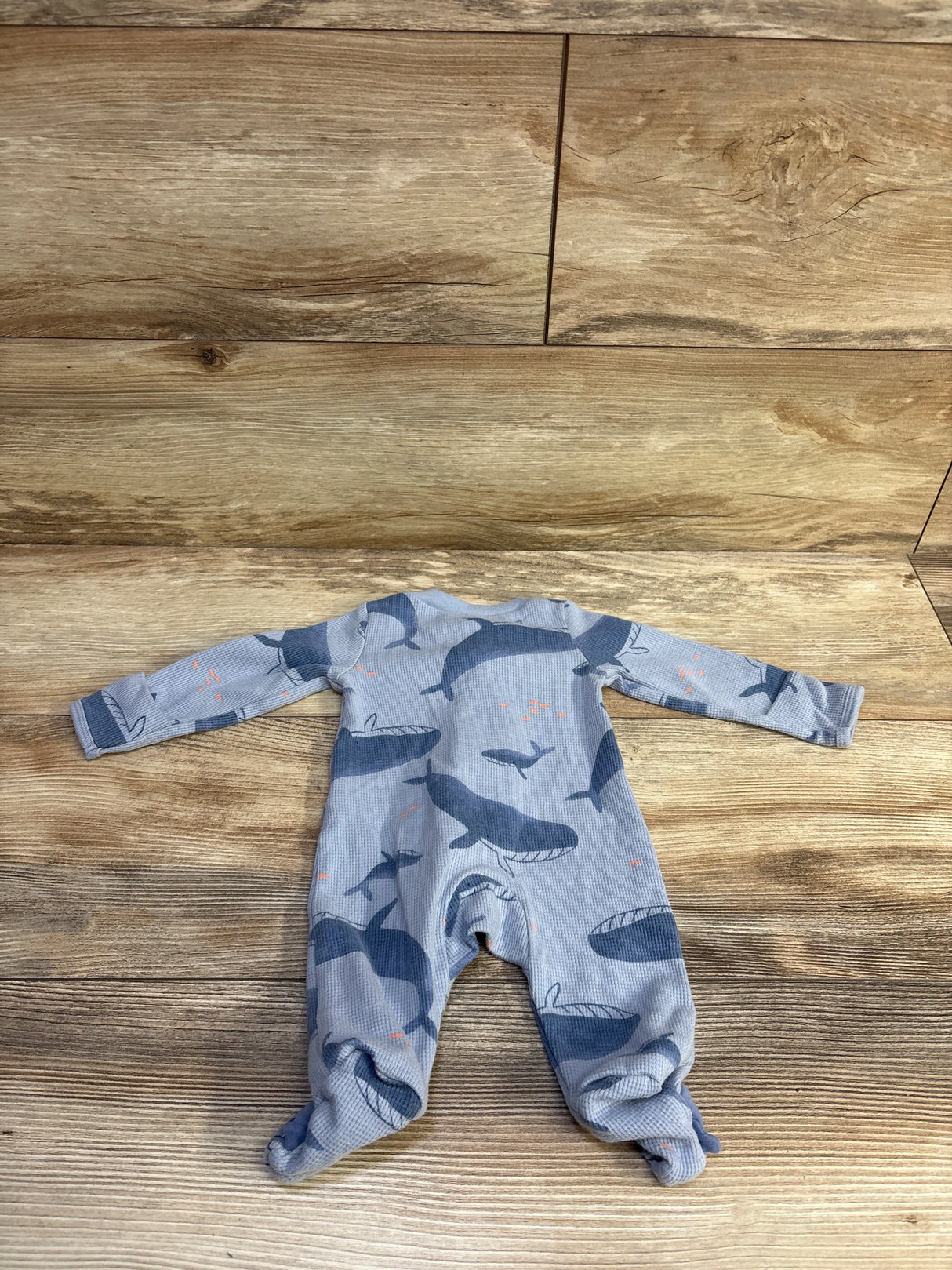 Flat lay of newborn blue waffle-knit footed sleeper showing whale print and long sleeves on wood background