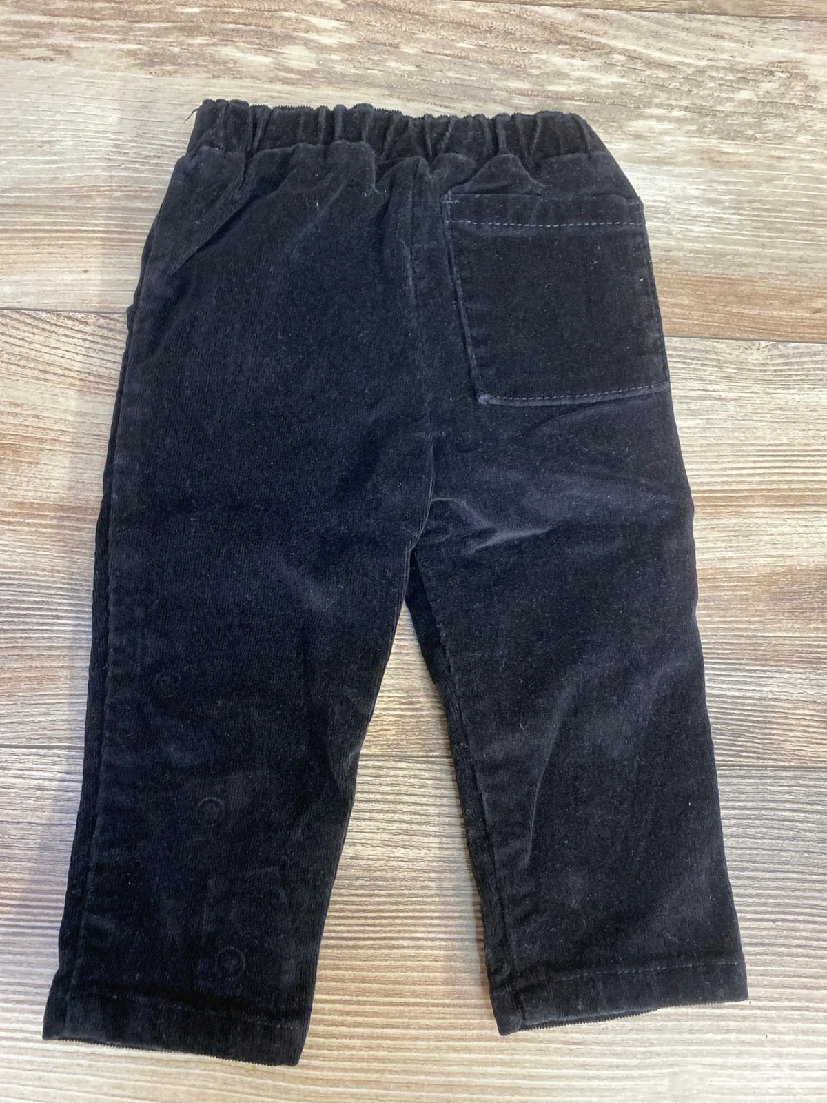 Black corduroy toddler pants with elastic waistband and back patch pocket on wooden floor
