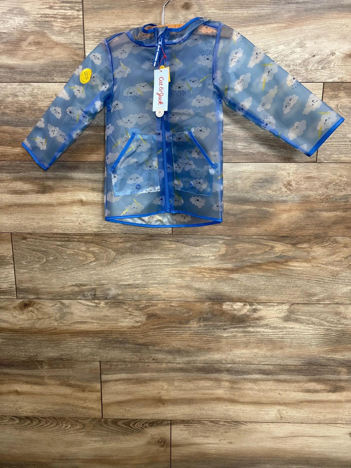 Blue kids raincoat with cloud and lightning print, hanging on a wooden background