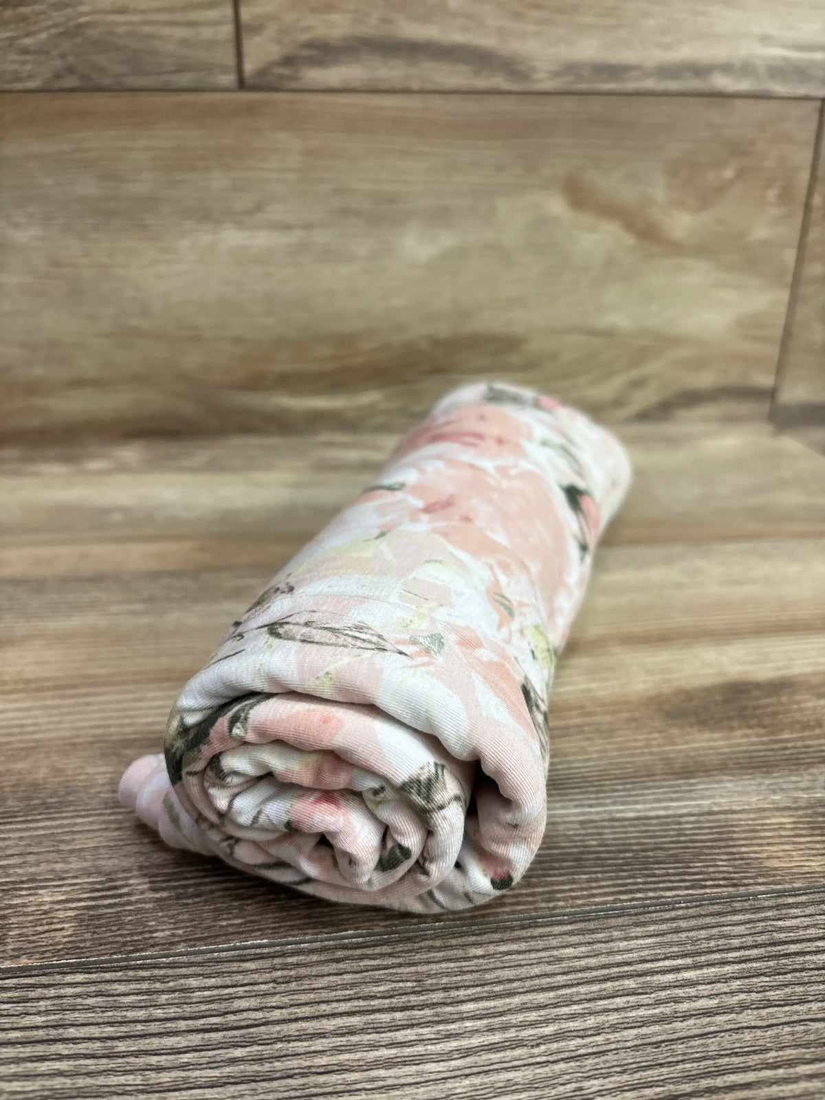 Rolled view of Posh P. bamboo swaddle blanket showcasing a pink floral pattern on a wood surface