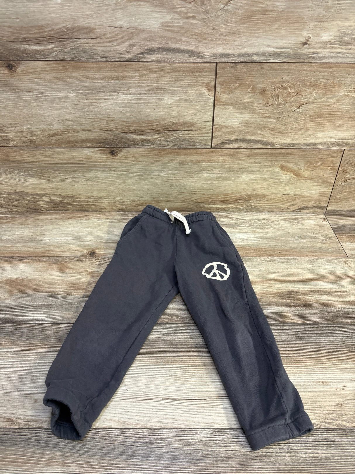 Flat lay of Tiny Whales grey joggers with drawstring waist, elastic cuffs and white left-leg graphic on wood background
