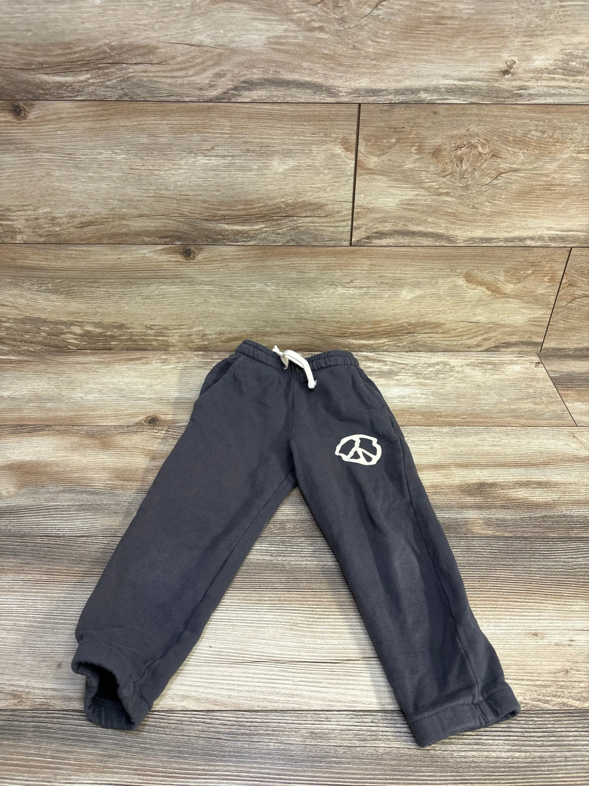 Flat lay of Tiny Whales grey joggers with drawstring waist, elastic cuffs and white left-leg graphic on wood background