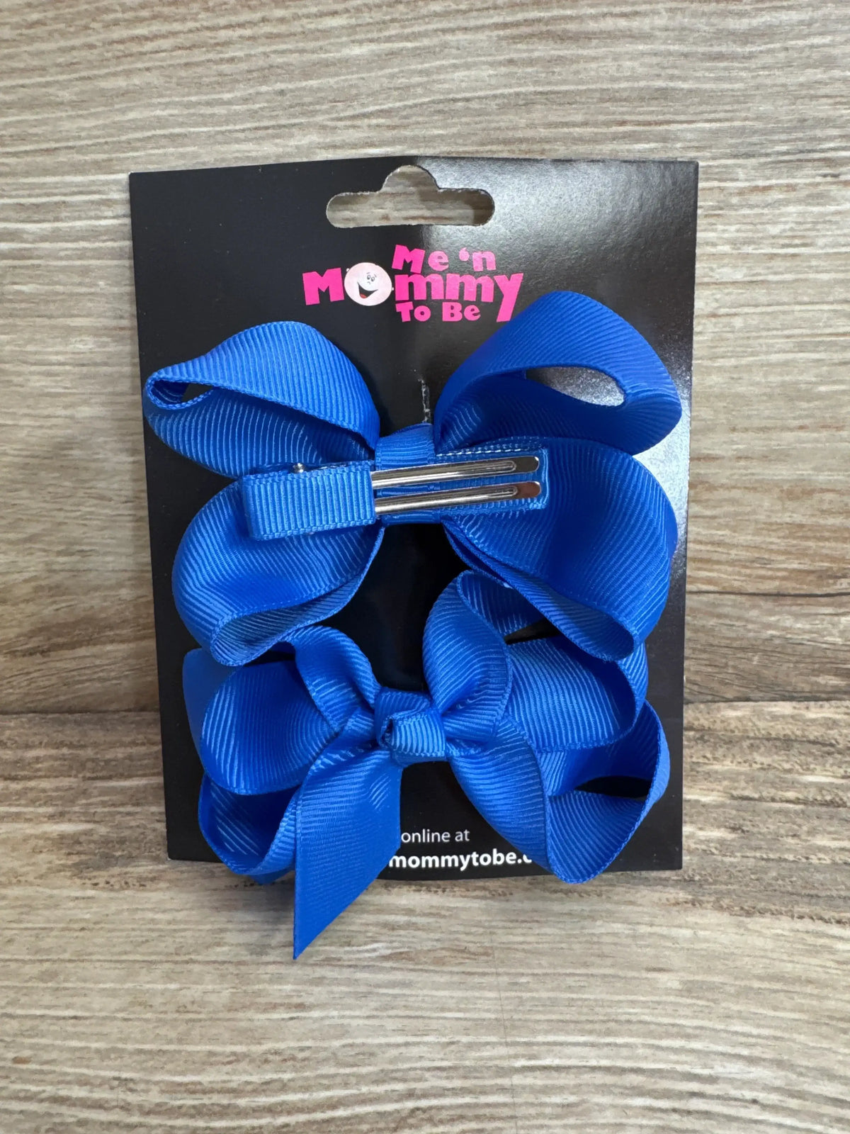 Front view of Me n Mommy To Be medium hair bows 2 pack in royal blue grosgrain ribbon on branded display card on wood plank floor