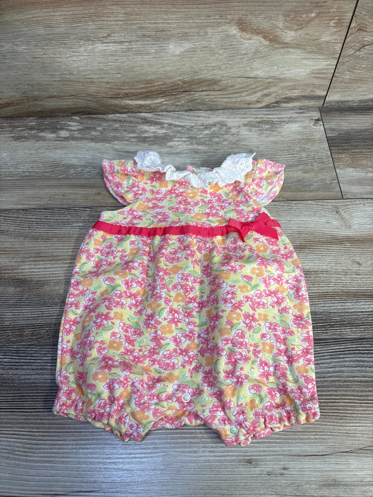 Front view of Laura Ashley floral shortie romper showcasing yellow floral print and ruffled neckline on a wood floor