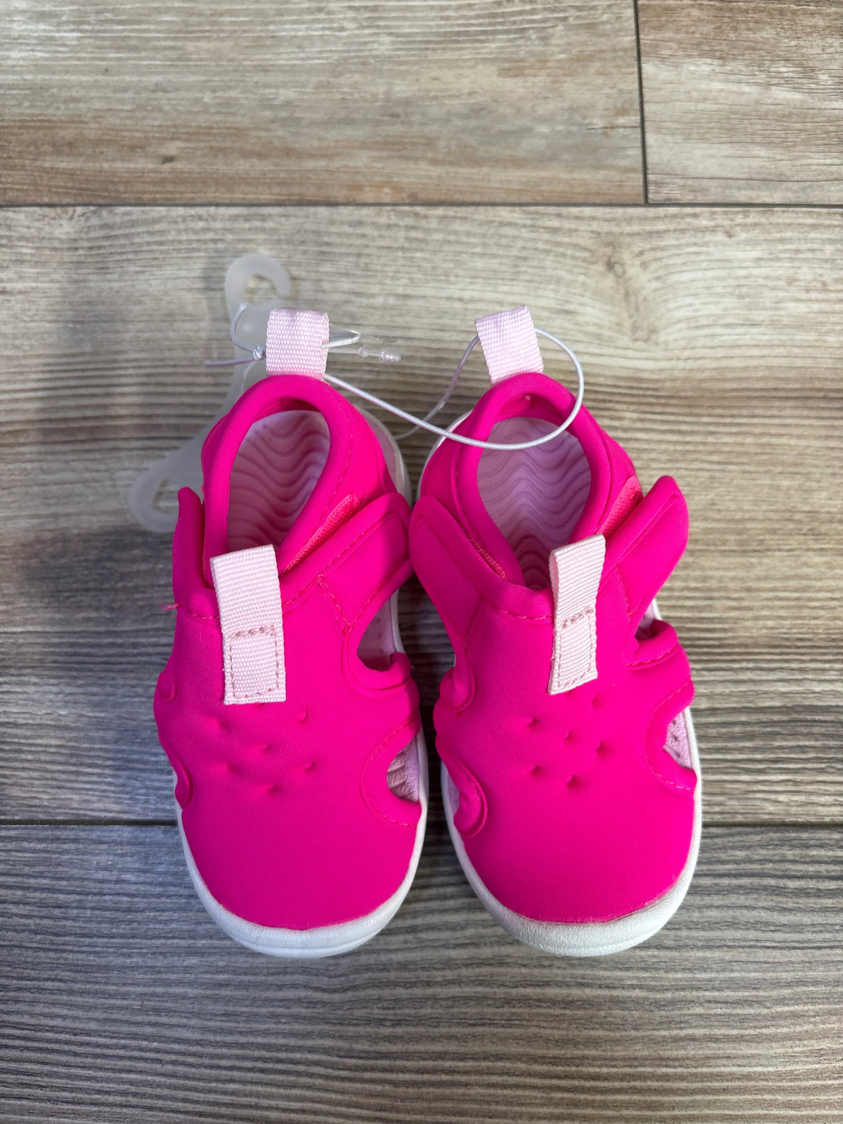 Top down view of pink toddler water shoes showing pull tabs, side cutouts and white soles on wood floor