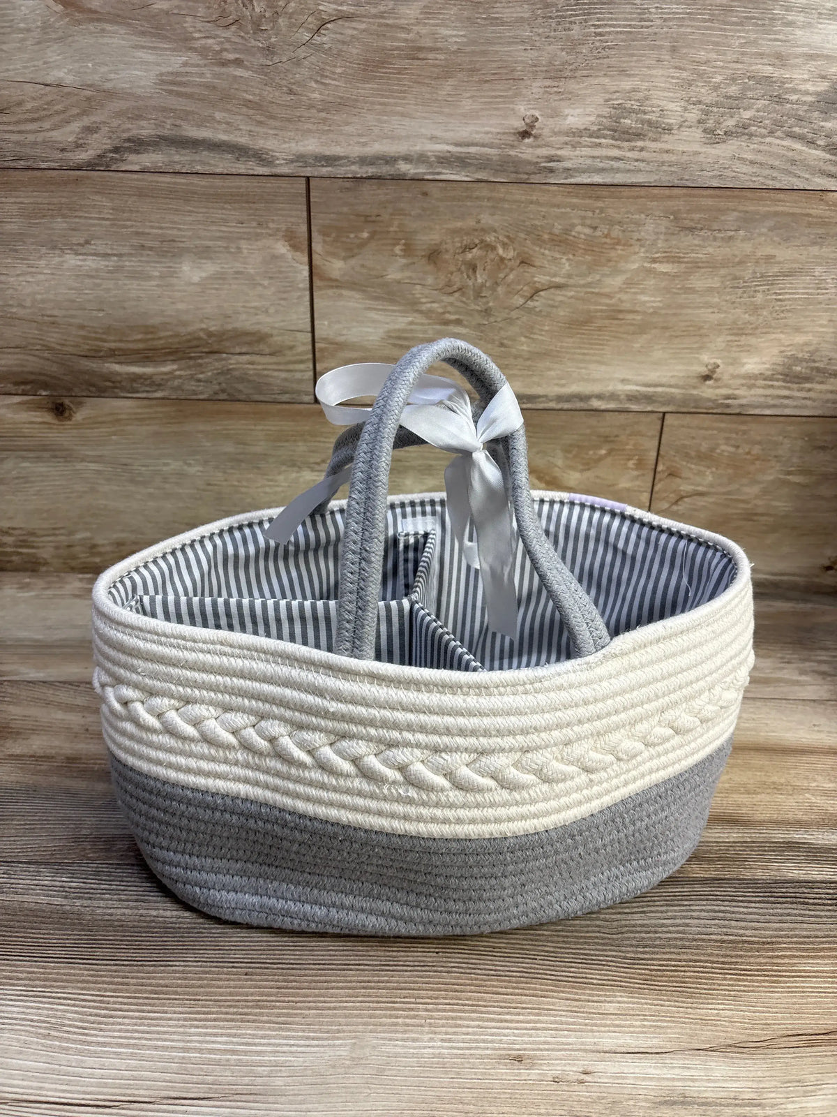 Three-quarter view of diaper caddy organizer with divided interior, braided rope trim and grey-and-cream color block on wooden backdrop