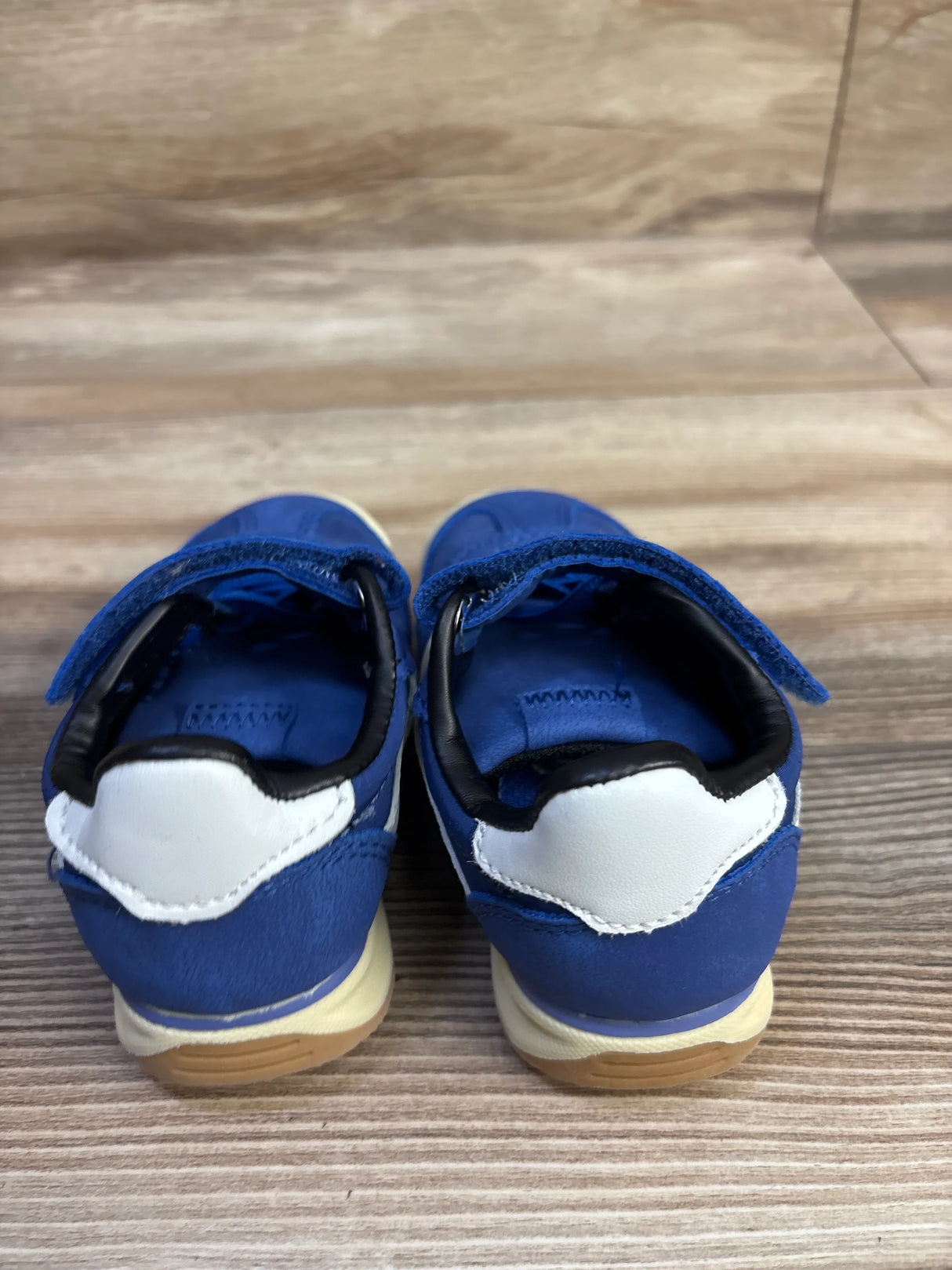 Rear view of blue Wonder Nation toddler sneakers showing white heel patch, Velcro straps, and gum soles on wood background