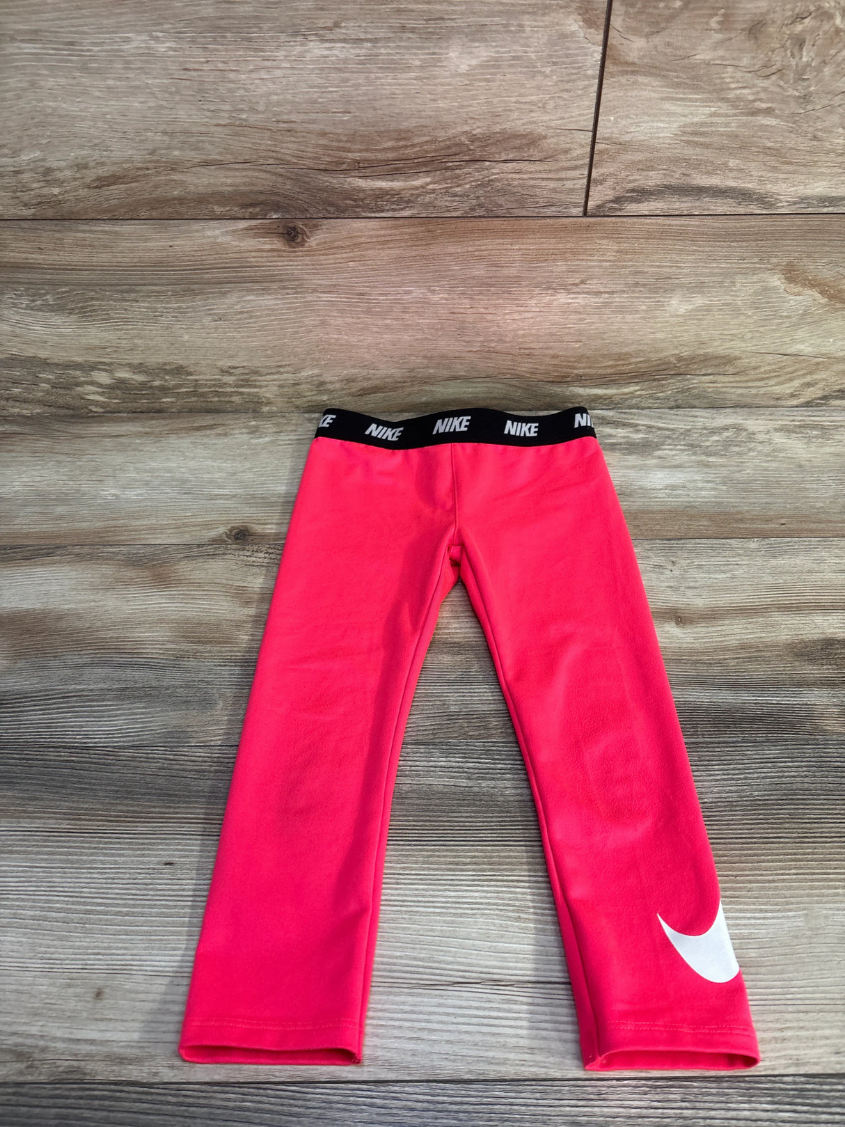 Front flat lay of girls pink Nike Dri-Fit leggings 4T showing black elastic NIKE waistband and white Swoosh on wood floor