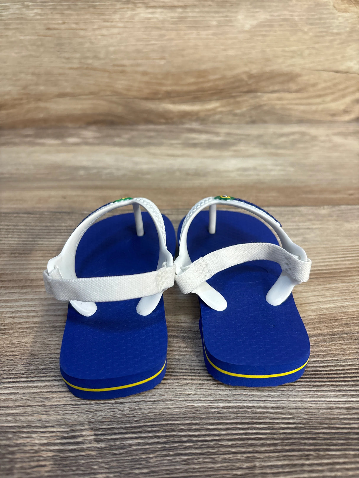 Blue toddler sandals with white straps and yellow accent on wood background