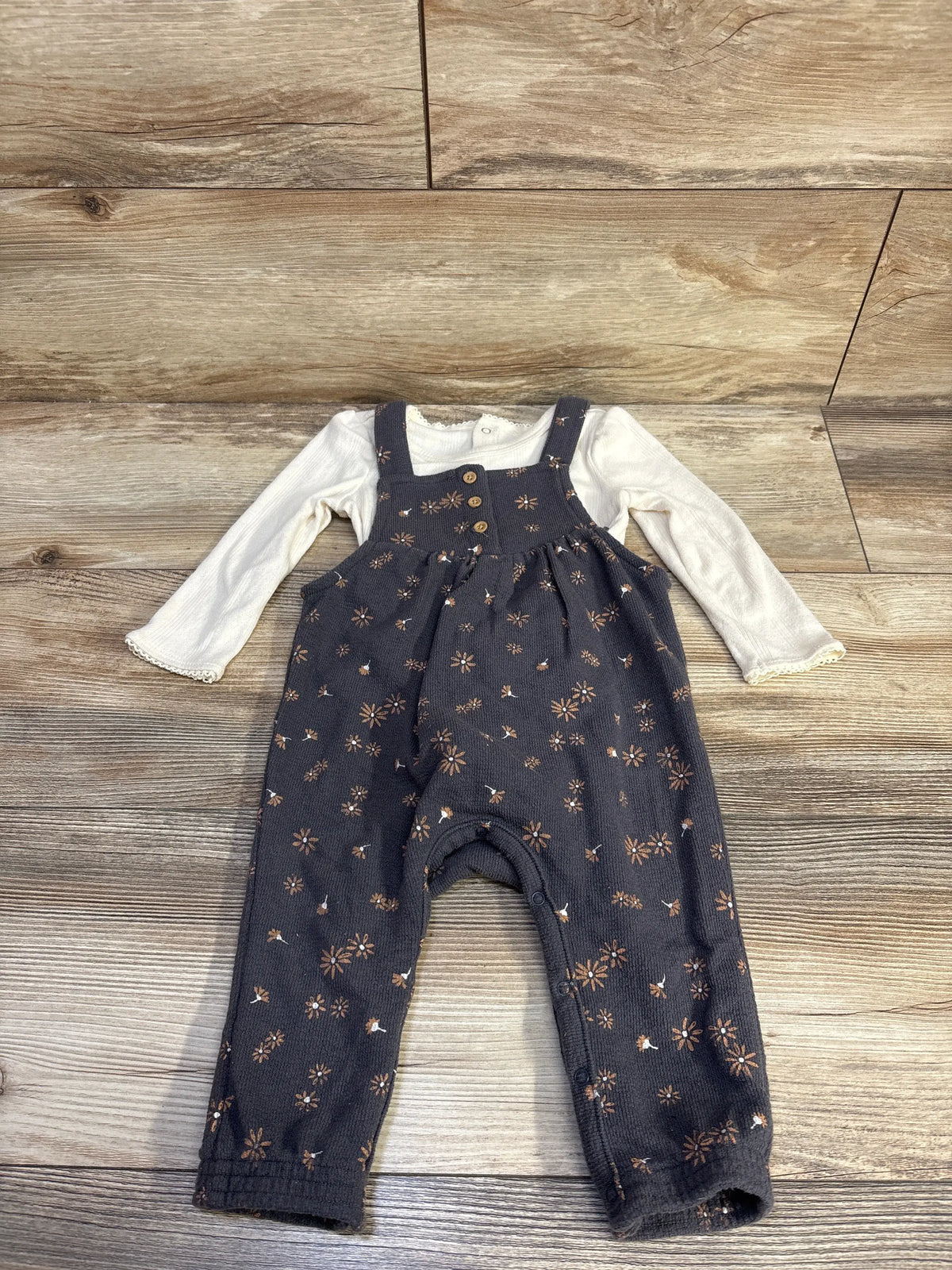 Front view of Grayson Mini two-piece set with ivory puff sleeve bodysuit and floral overalls on wood flooring