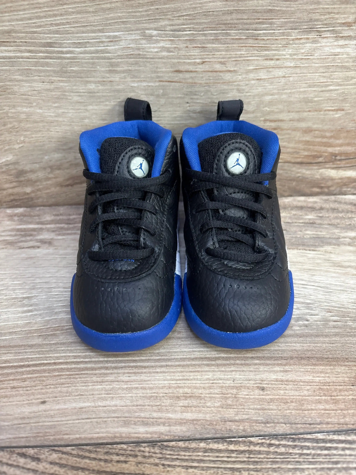 Front view of toddler Air Jordan Jumpman Pro BT sneakers showing black tumbled leather, blue lining and blue midsoles on wood background