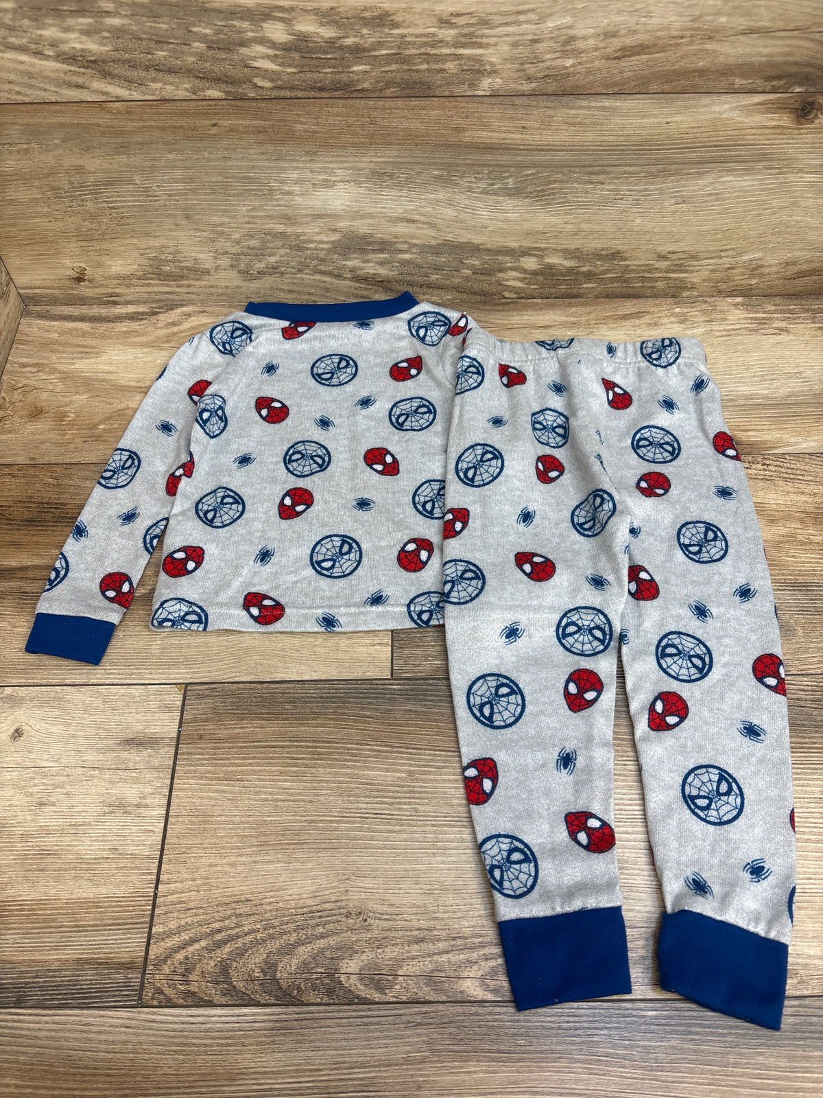 Flat lay of Marvel 2pc Spider-Man pajama set in grey showcasing navy cuffs and Spider-Man print with a wood floor background