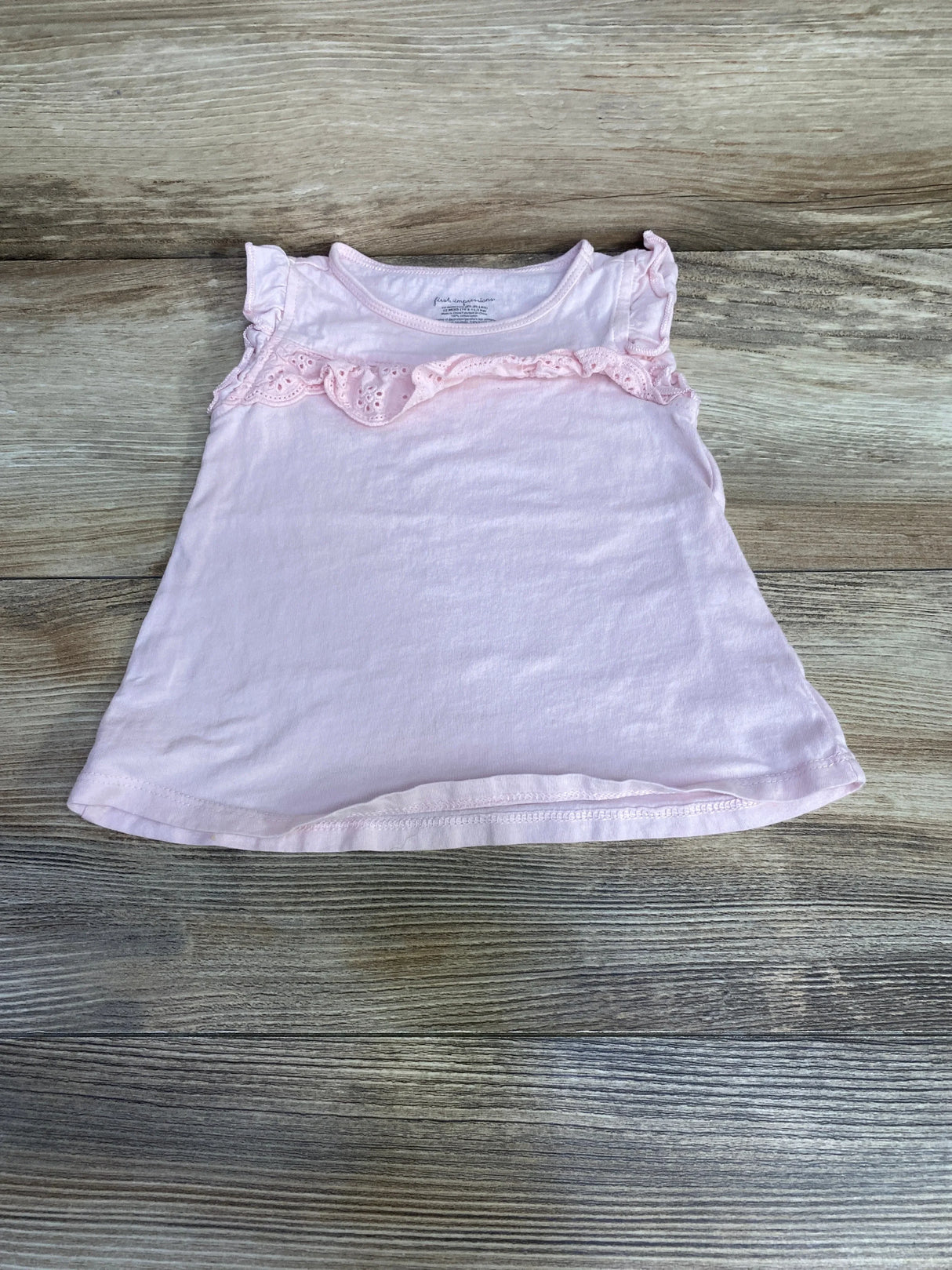 Flat lay pink eyelet ruffle toddler shirt, size 12m, showing eyelet trim and flutter sleeves on light wood