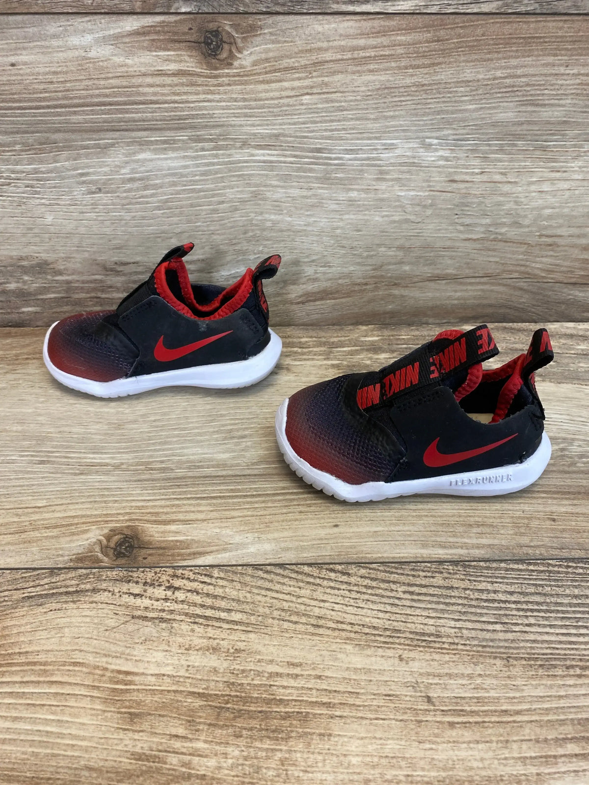 Side and angled views of Flex Runner TD sneakers showcasing black and red gradient slip-on uppers with white soles on wood