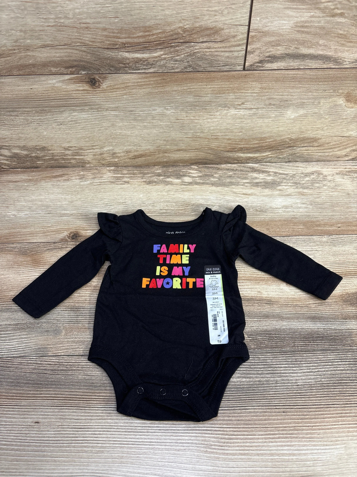Black long-sleeve baby onesie with colorful text 'Family Time Is My Favorite' and ruffle shoulder details