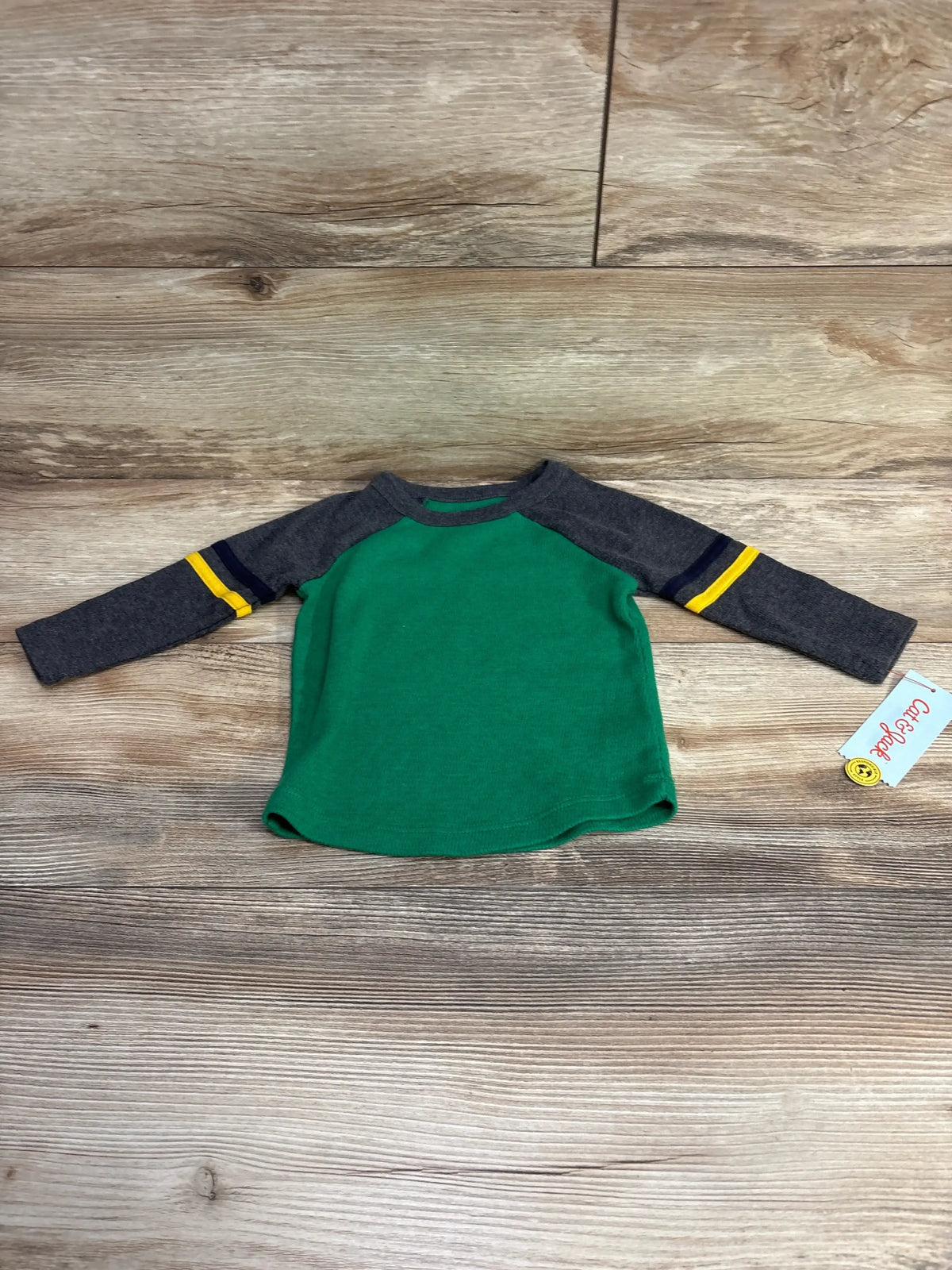 Green and gray toddler long sleeve shirt with yellow and navy stripes on sleeves lying on wooden floor