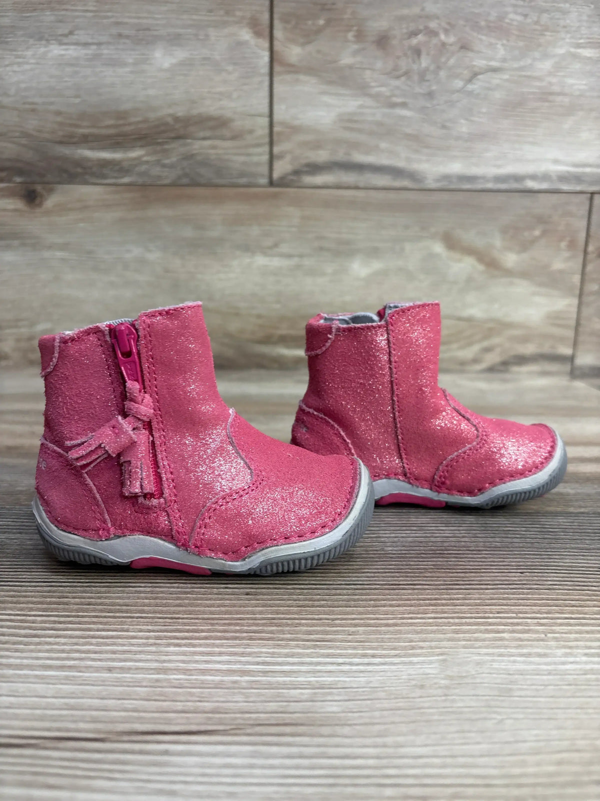 Pair of glittery pink toddler boots with side zippers and gray soles on wooden floor