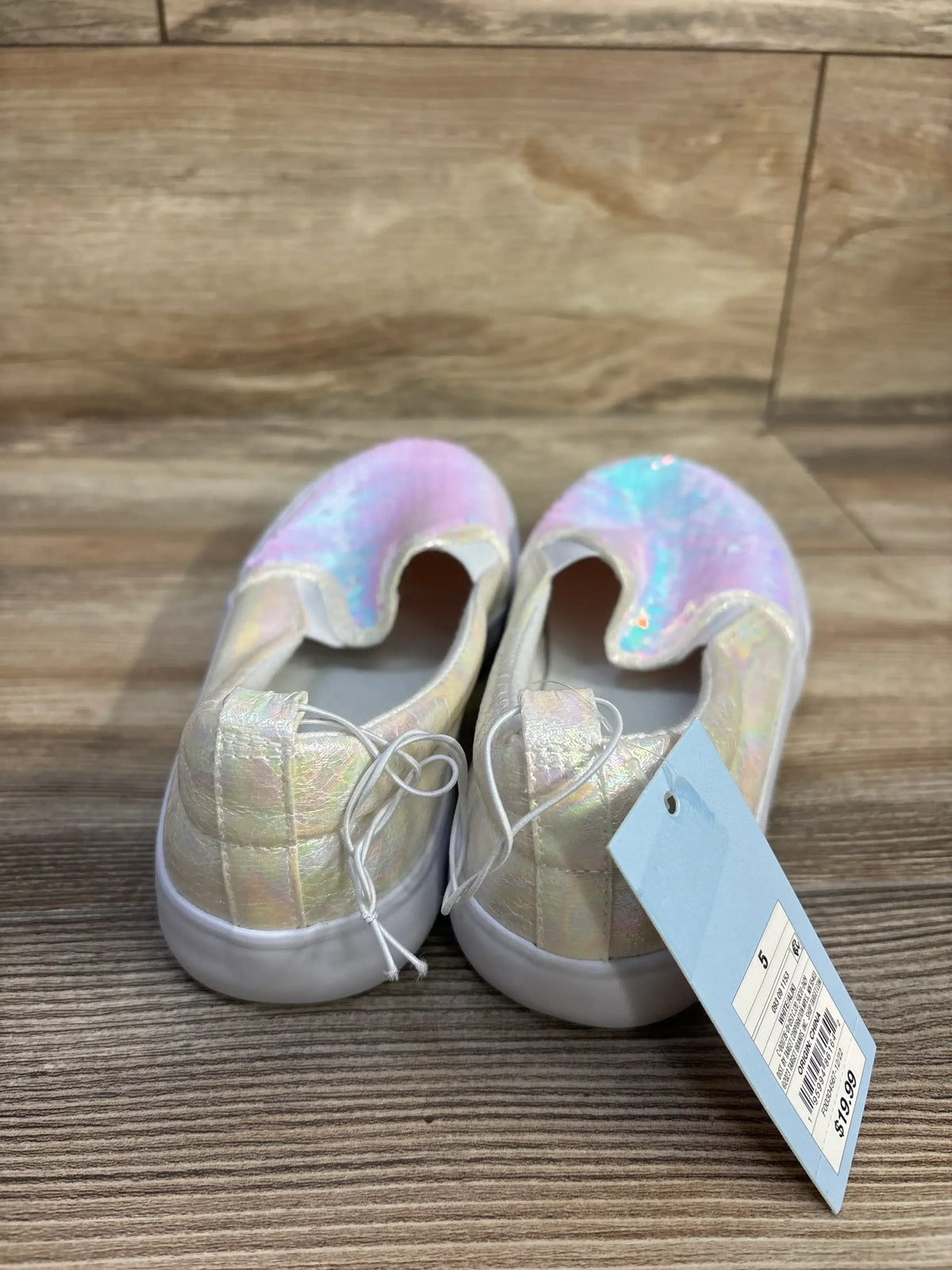 Rear three-quarter view of Cat & Jack Aliki slip-on sneakers showcasing iridescent pastel sequined uppers and white soles on a wood floor