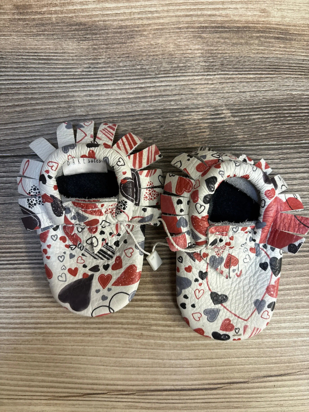 Baby moccasins with heart pattern in red, gray, and black on wood background