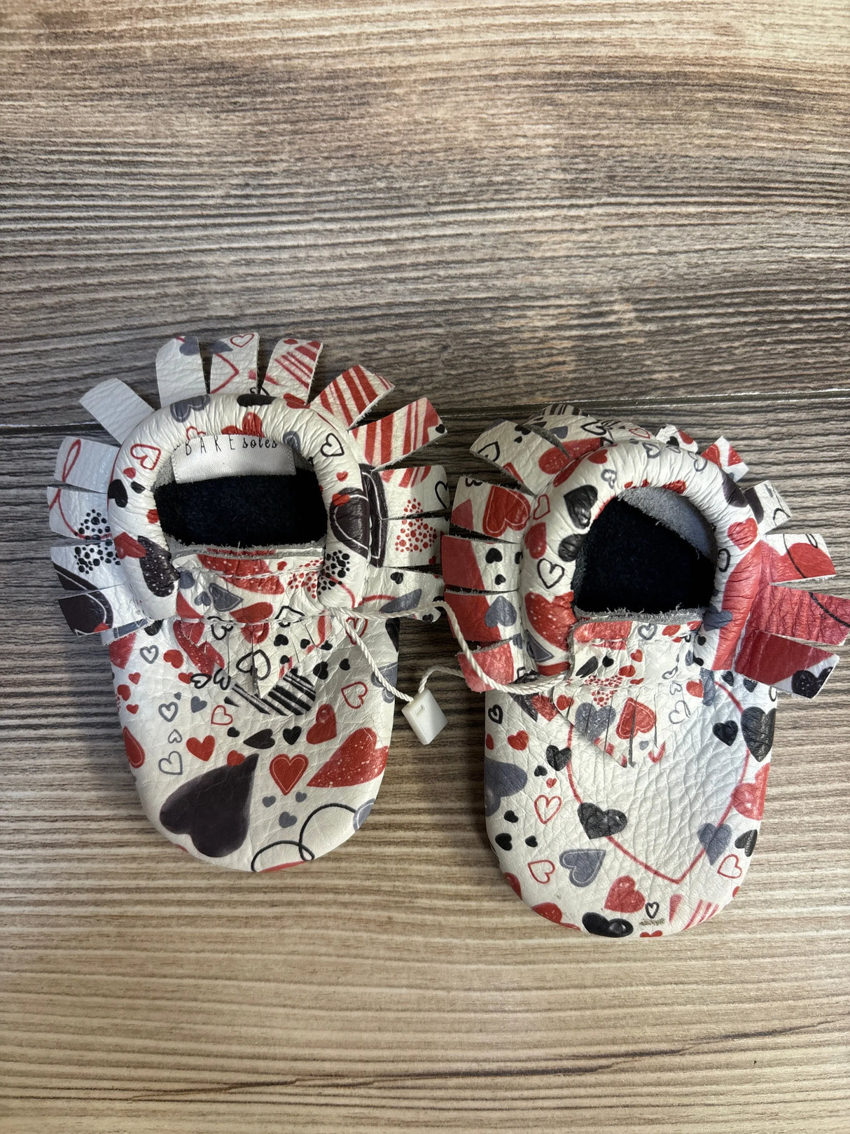 Baby moccasins with heart pattern in red, gray, and black on wood background