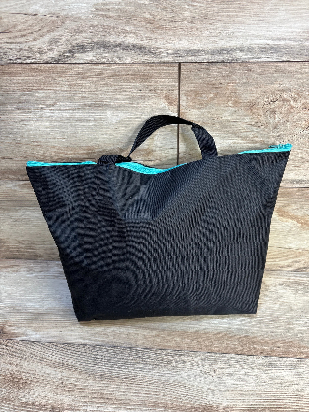 Black tote bag with teal zipper and handle on wood floor, kids gear accessory