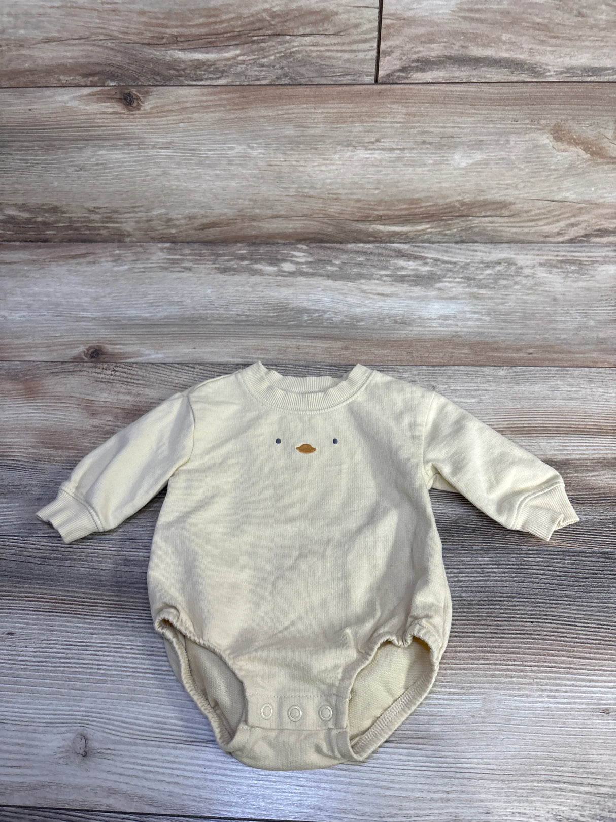 Flat lay of yellow baby bubble romper with embroidered duck face and three snap crotch closures on wood background
